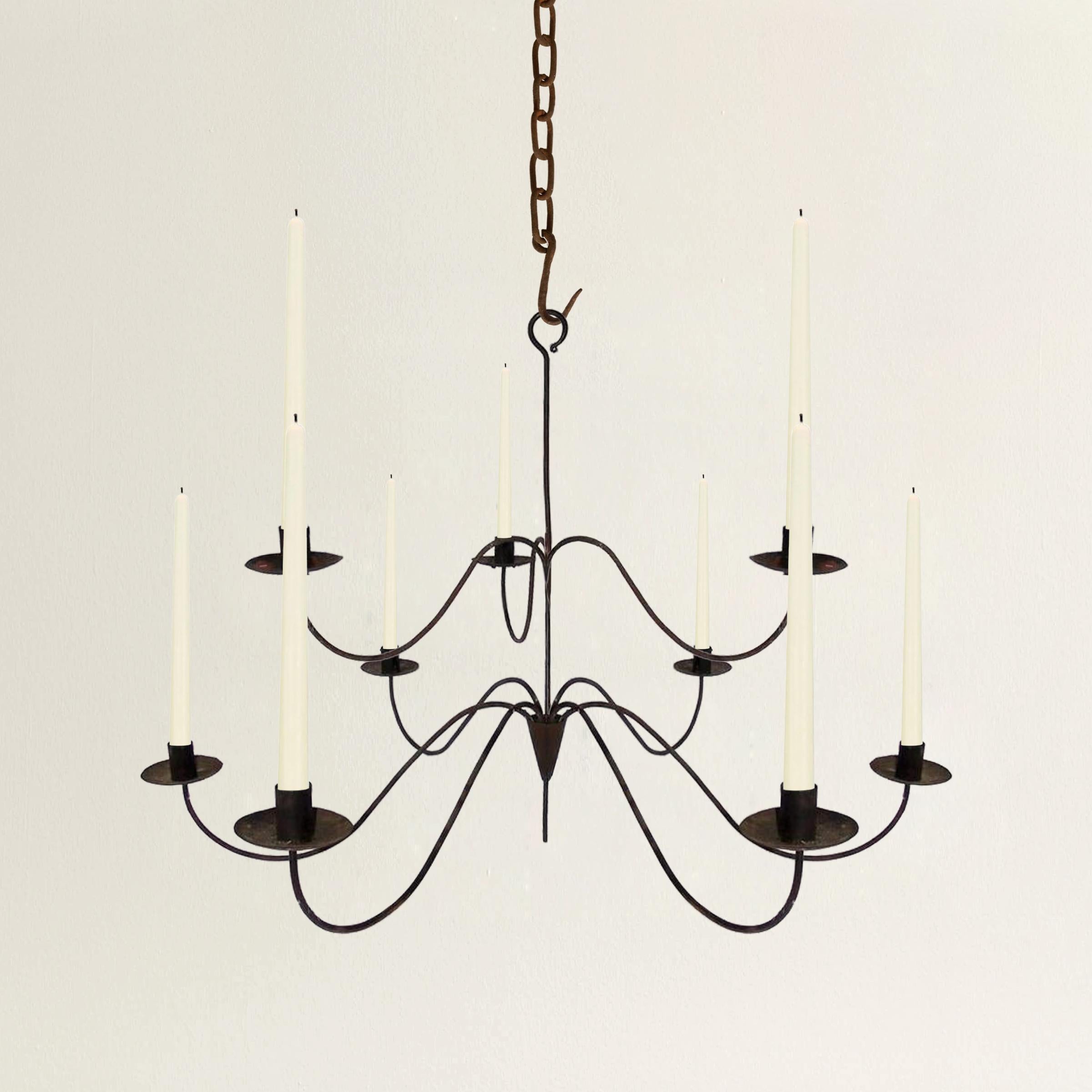 A whimsical 19th century American wrought iron chandelier with nine scrolled arms, consisting of six in a circle on the bottom tier, and three around the top tier. The fixture originally used candles, and has never been electrified.