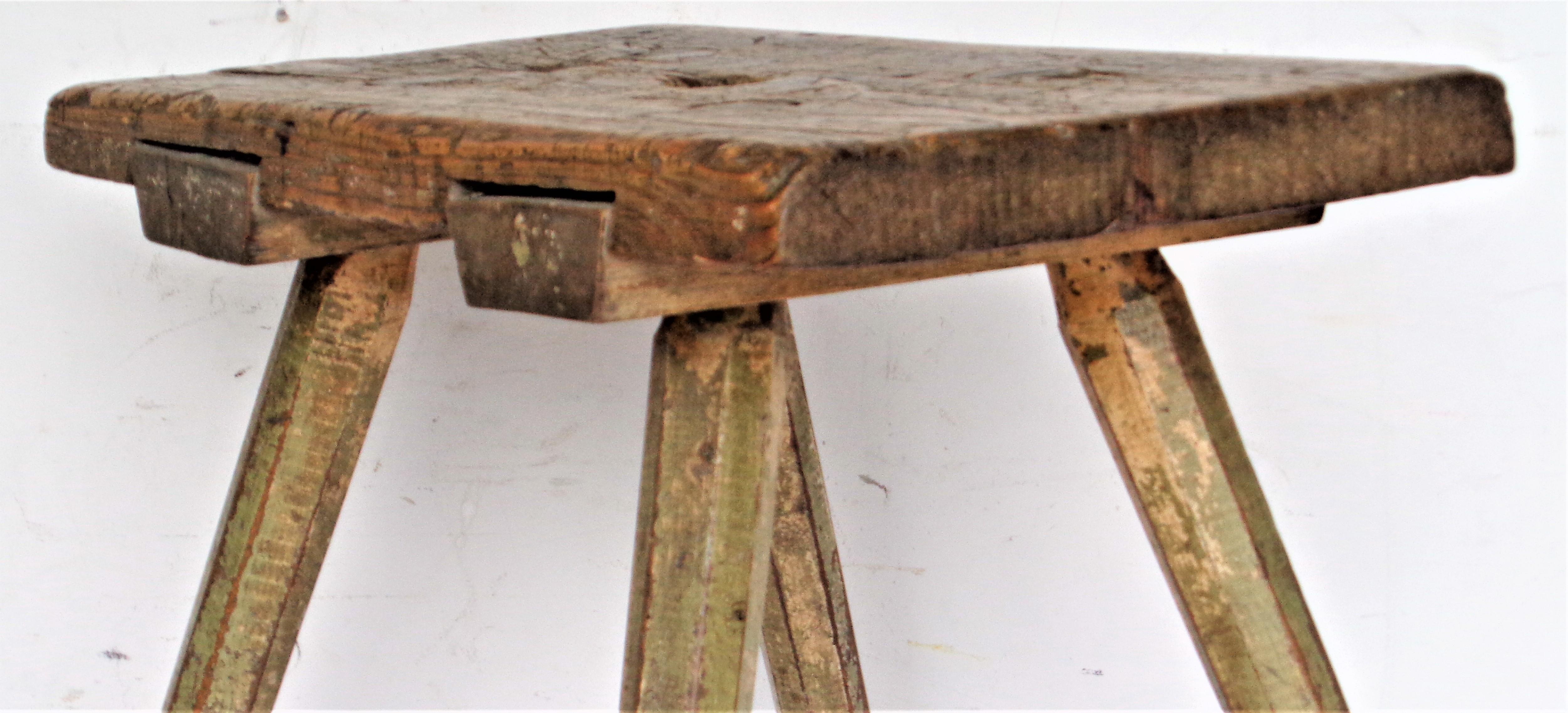 19th century American country hand crafted primitive work stool with four chamfered splayed legs with early through pegged construction. Exceptionally beautifully aged original warm pea green and cream painted surface to legs and underside of seat.