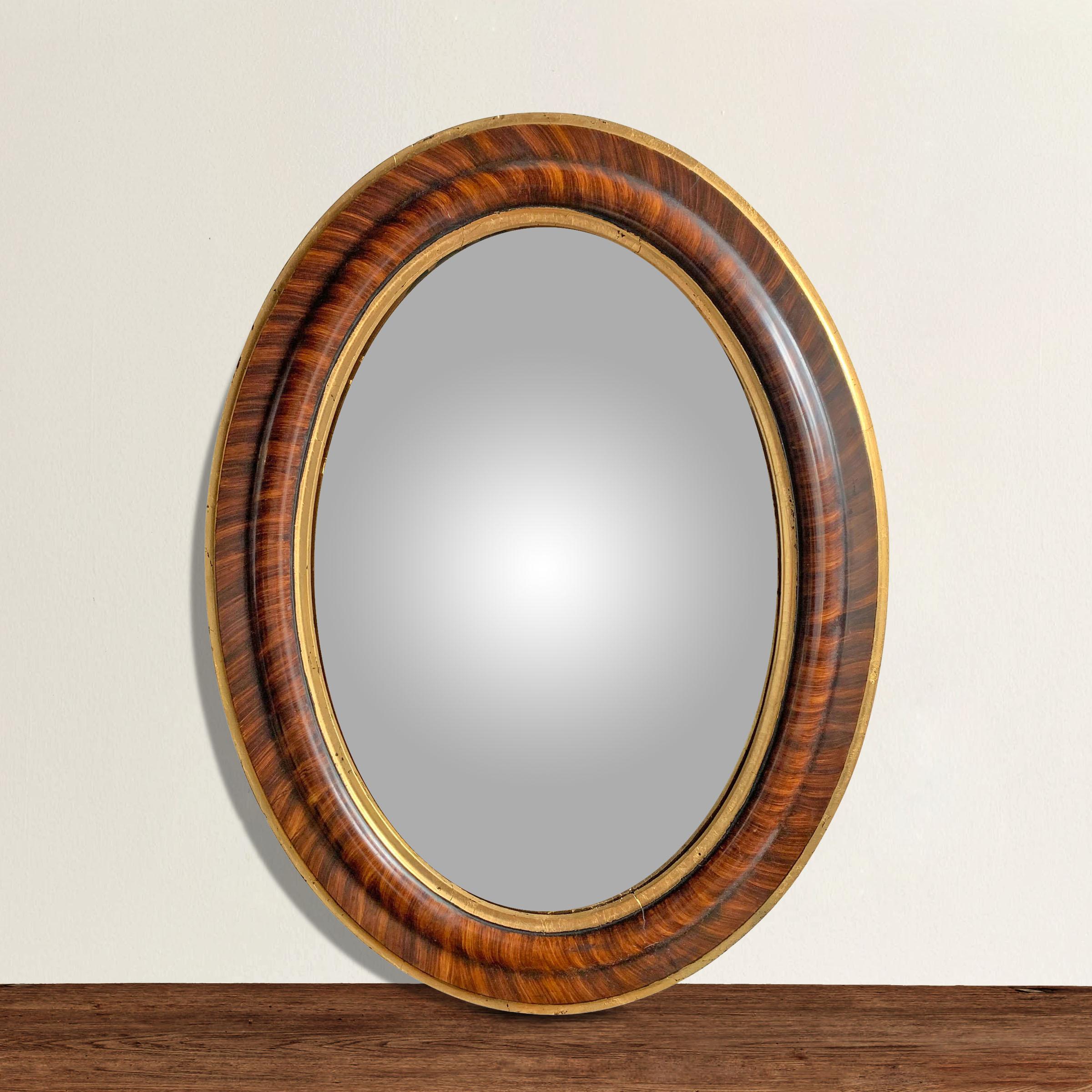 A 19th century American faux grain painted oval framed convex mirror with a hand-applied gold leaf inner and outer edge.