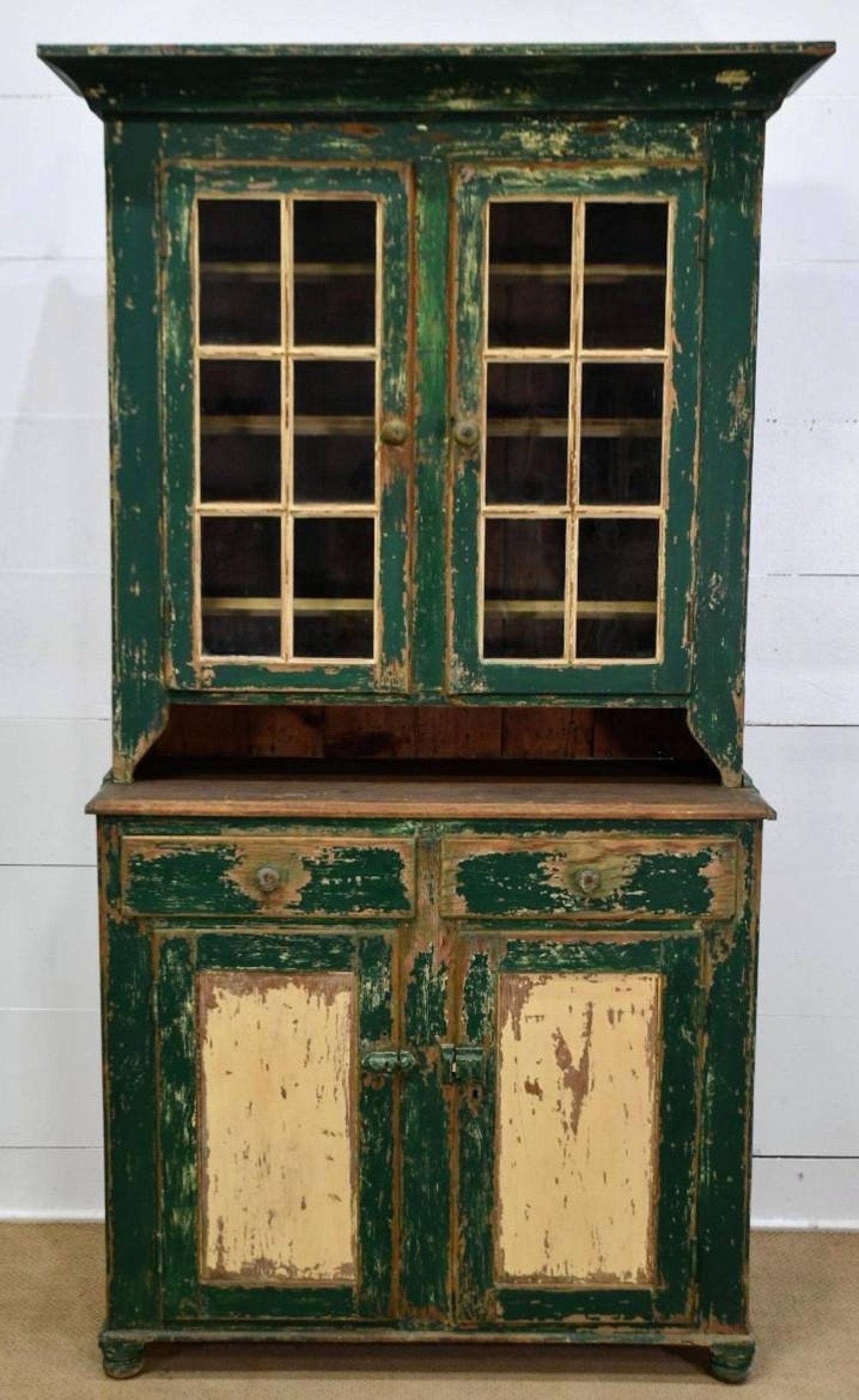 A early American farmhouse green painted pine stepback cupboard.

Born in Pennsylvania during the first half of the 19th century, rustic hand-crafted solid wood construction, two-piece, having a simple cornice over a tall pair of glazed glass