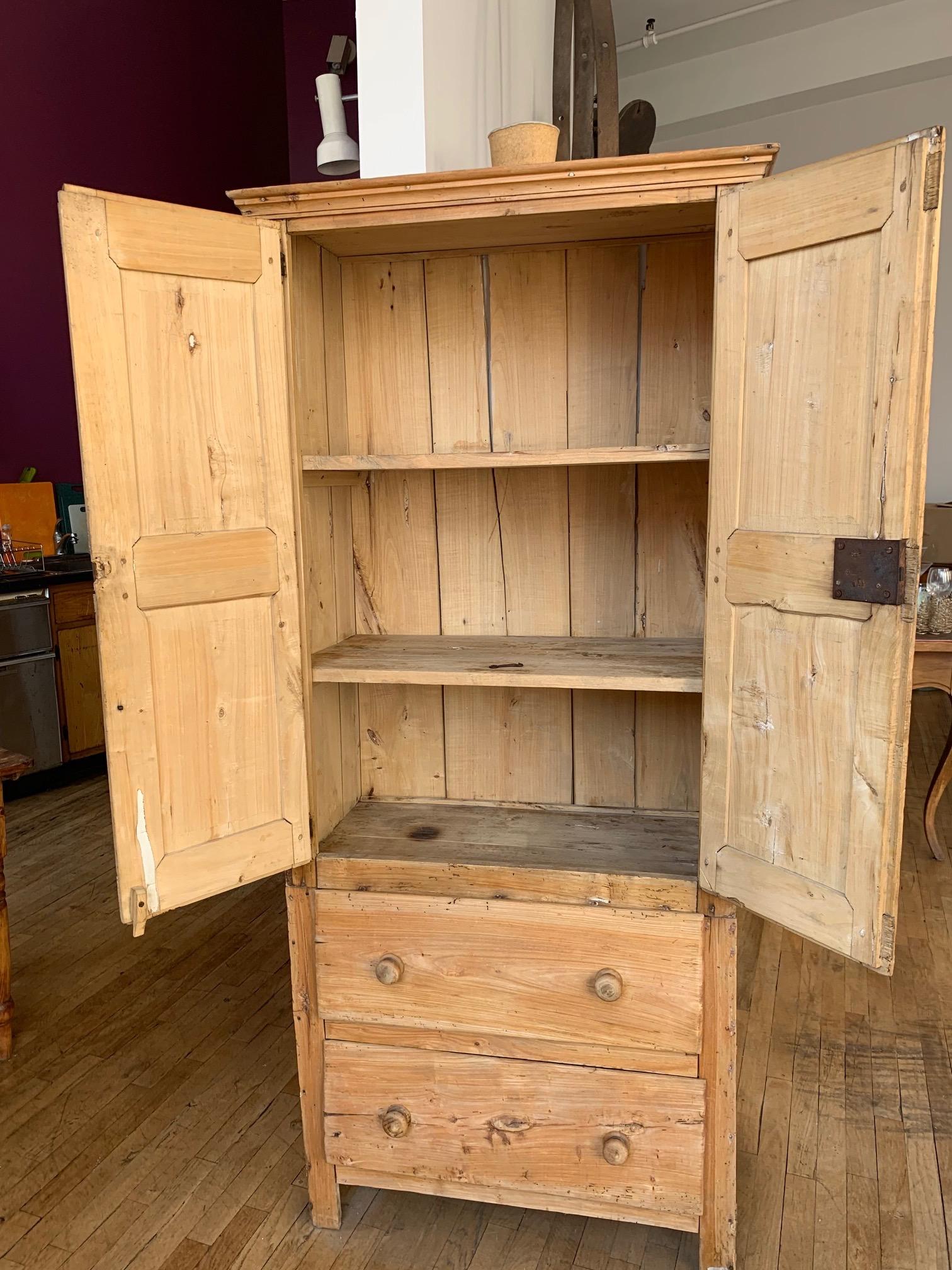 19th century American pine armoire with drawer. This armoire offers different types of storage; The cabinets themselves open up to reveal three shelves, however additional storage is provided in the two drawers which rest below the shelving unit.