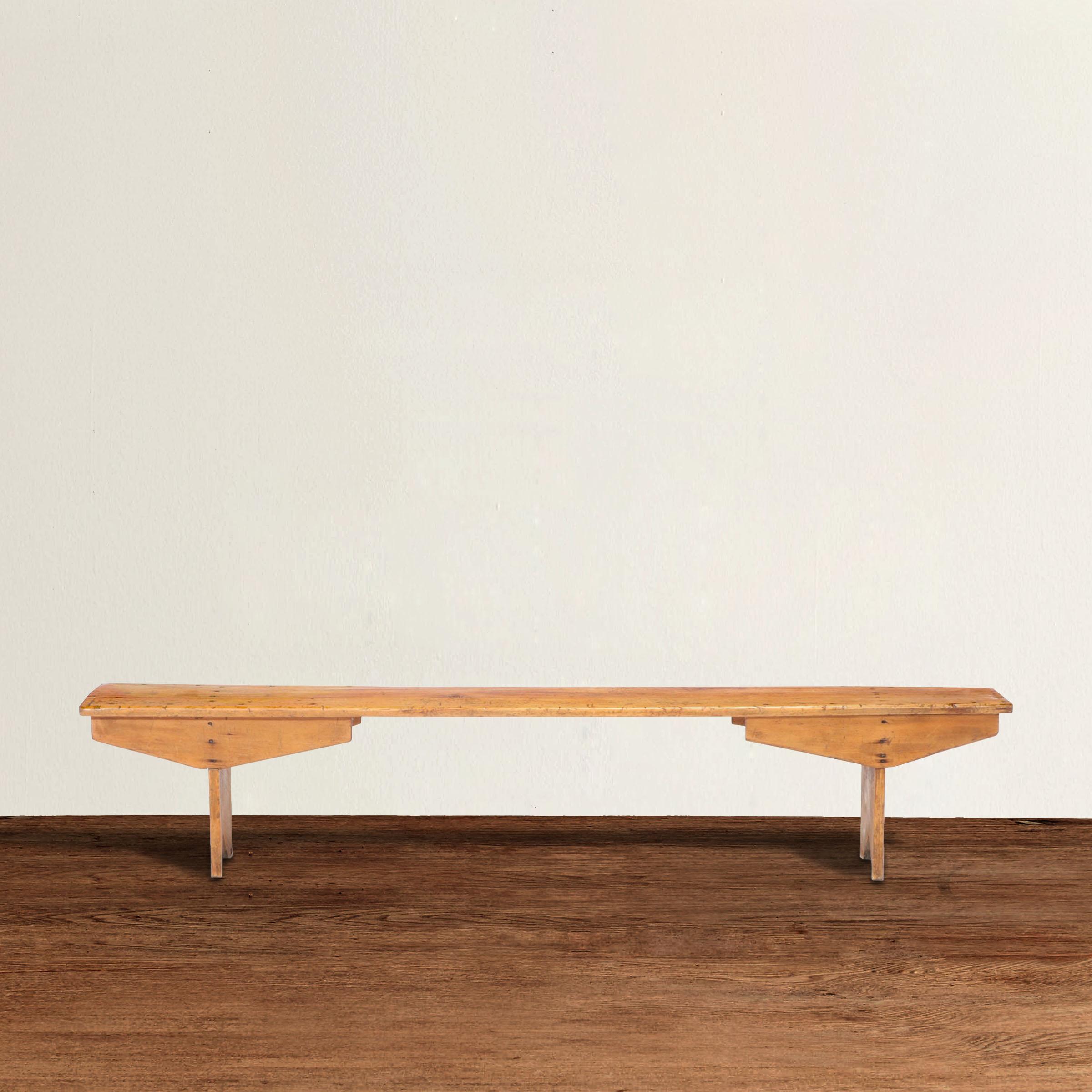 A chic and modern-in-spirit 19th century American pine single plank-top bench with simple legs and exaggerated wide spandrels.