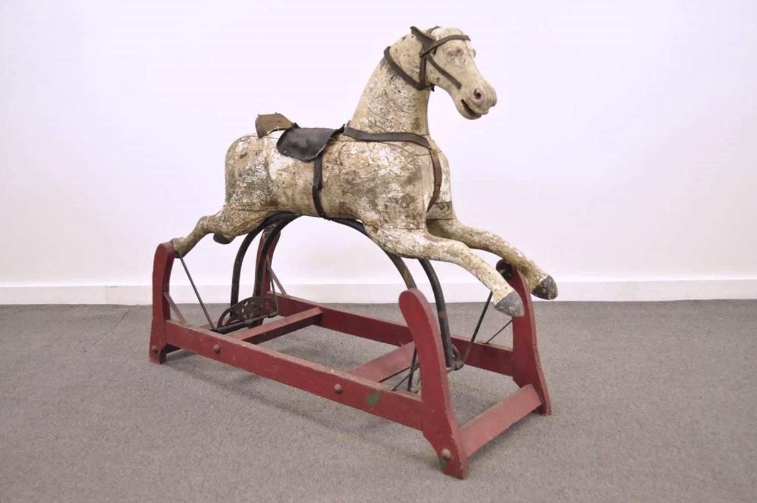 Antique American primitive handmade gliding hobby horse. The piece features a carved wood horse, red painted wood base, cast iron hardware with star accents, and leather straps and saddle. The attention to detail is readily apparent, even after 100+