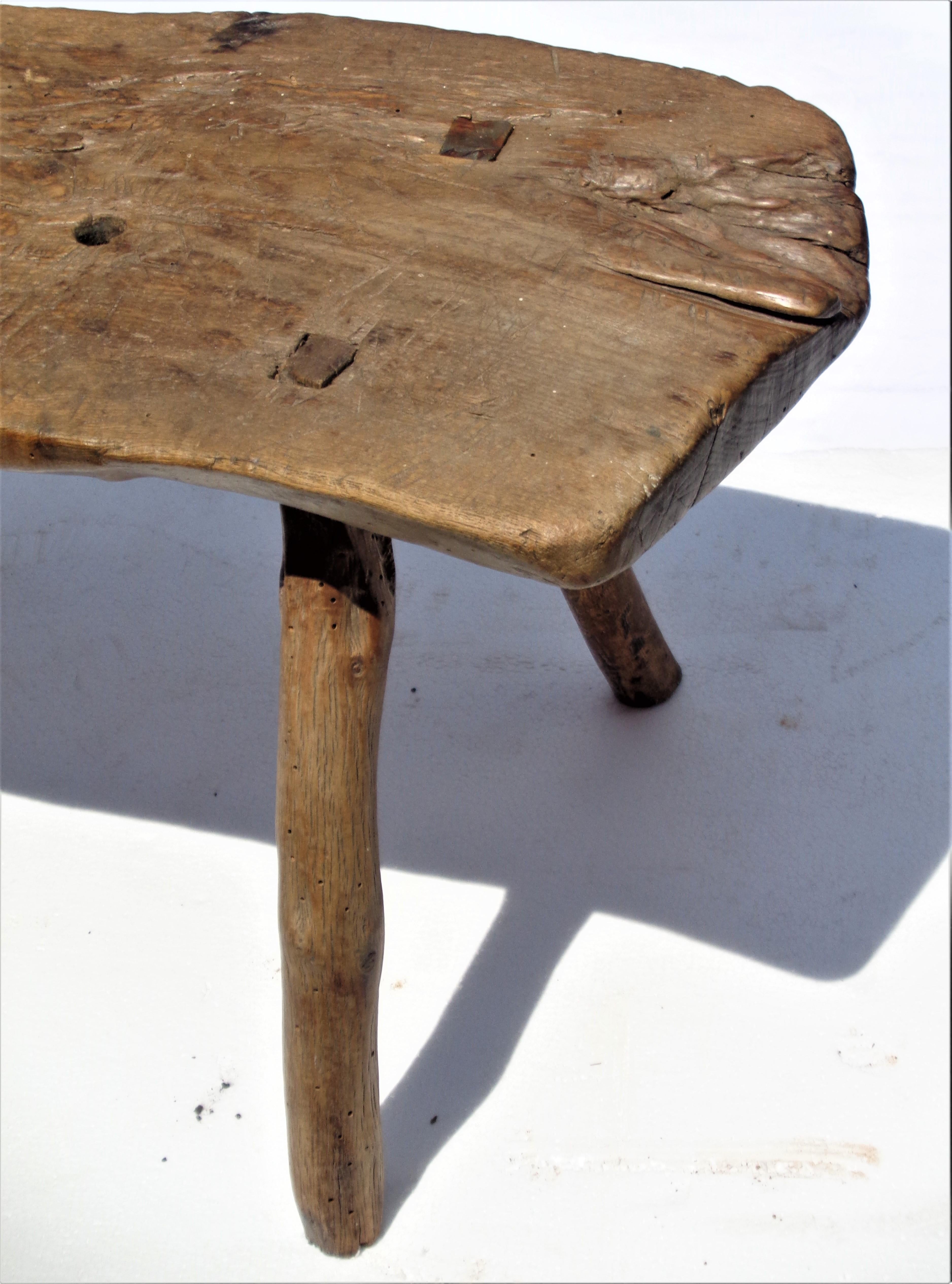 Antique American country primitive three legged work stool with early pegged through construction in original beautifully aged natural color. The thick free form tree wood slab top with genuine wear from well over a hundred years of actual use