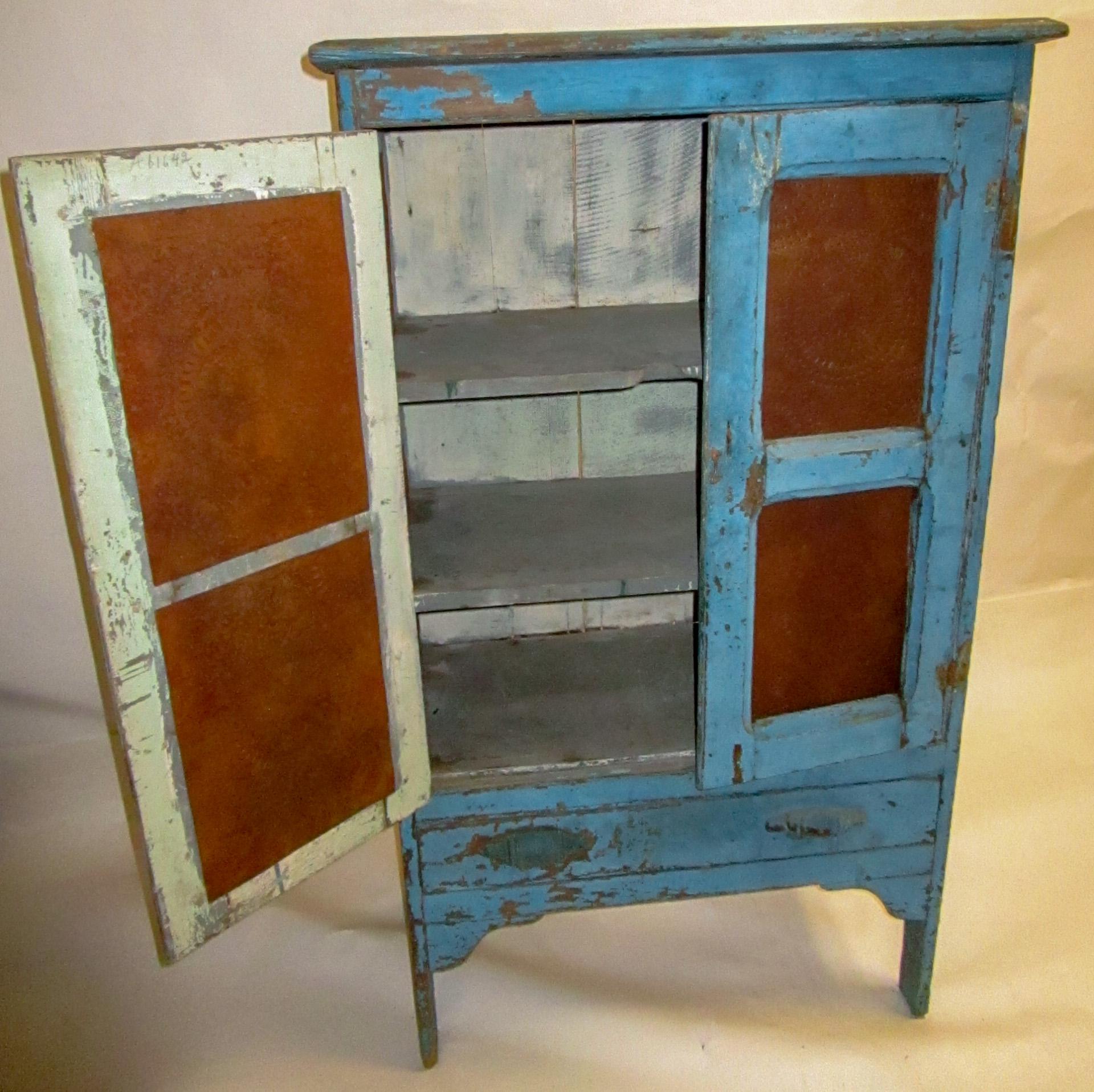 A truly American Southern piece, this rustic wooden pie safe features pierced tin inserts in the double doors and on the sides. Other features include two shelves, primitive hardware and wonderful old distressed blue paint. The nicks and scrapes and