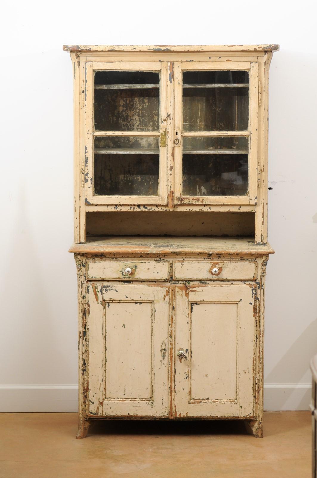 A 19th century American rustic painted wood cabinet with glass doors. Born in North America during the 19th century, this handsome cabinet charms us with its distressed finish and rustic appearance. Presenting a thin cornice overhanging two glass