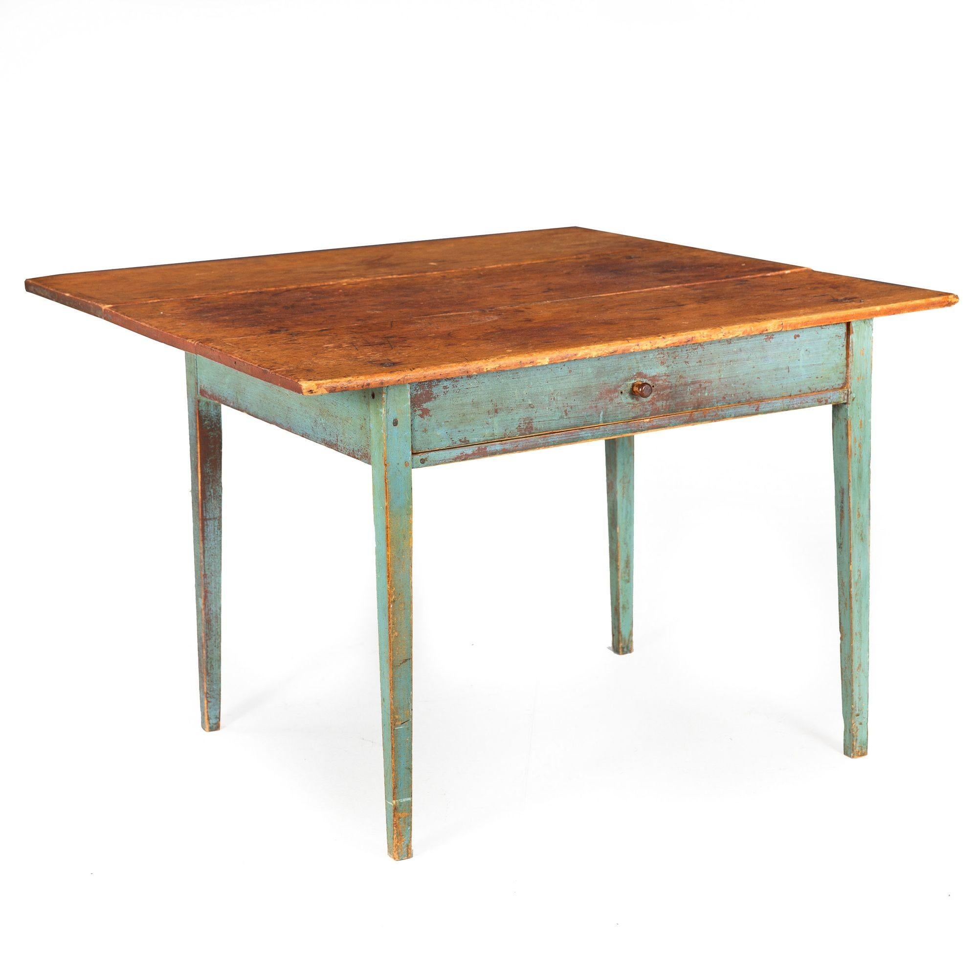 A delightful early 19th century work table, it features a single drop leaf that falls neatly behind the table over one original hinge (one replaced). Crafted out of several boards of scrubbed pine, there are trace remnants of a nearly maroon-red