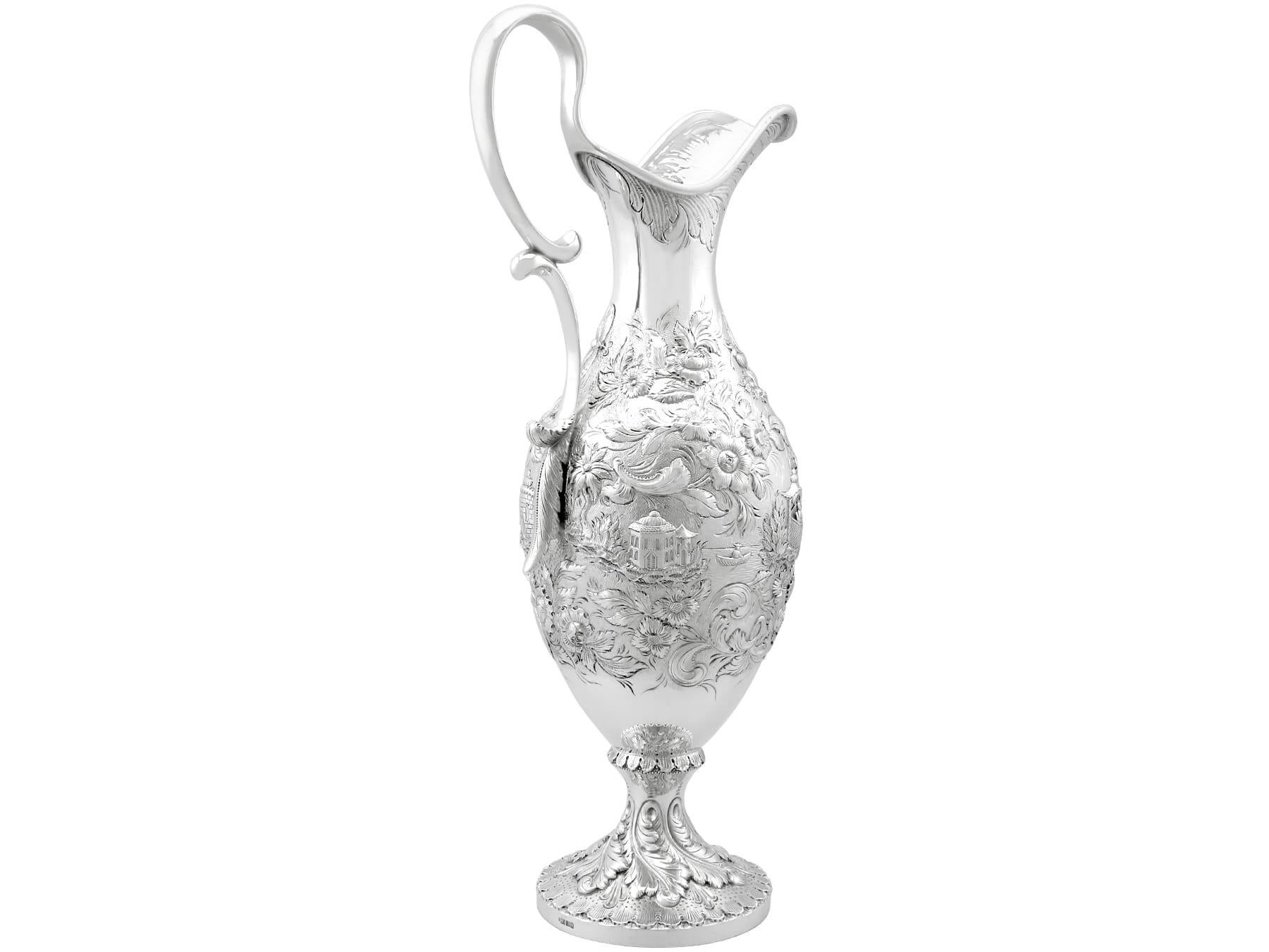 This magnificent antique 19th century American silver claret jug has baluster form onto a plain circular spreading foot.

The body of this antique jug is embellished with exceptional chased decoration, displaying a Chinoiserie style landscape and