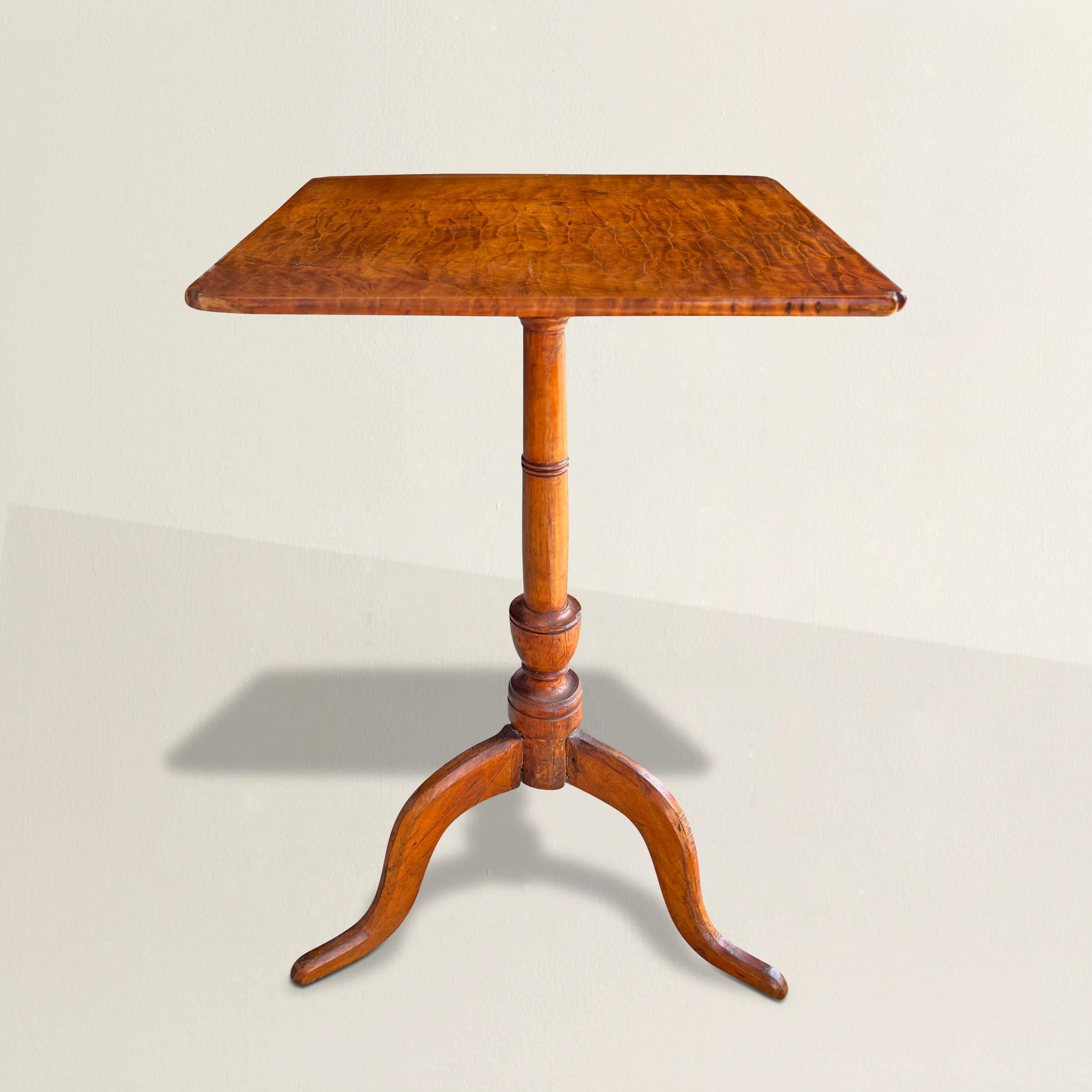Transport yourself to the early 19th century with this exquisite American Colonial candle stand, a magnificent fusion of artistry and functionality. Crafted from lively grained tiger maple, the top exudes a captivating allure, while the turned maple