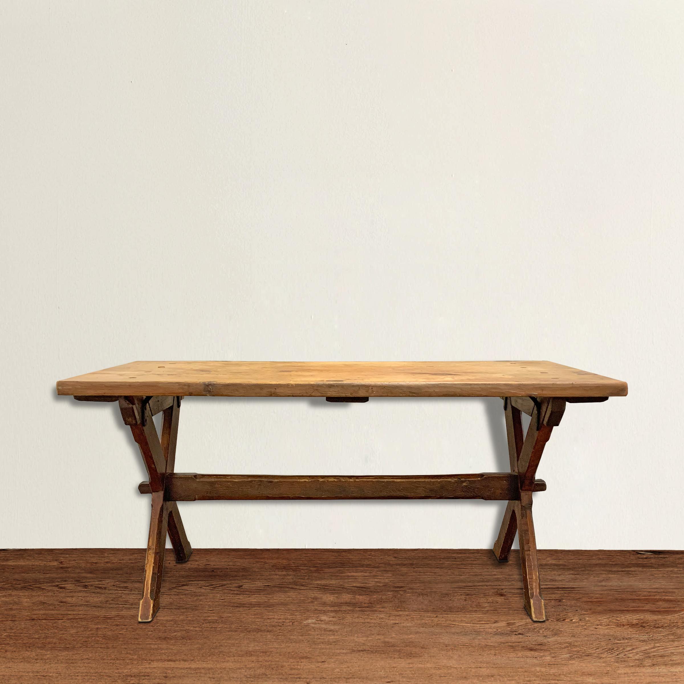 A wonderful 19th century American pine trestle table with an X-form base with chamfered legs, and a stretcher that's pegged on each end. Traces of the table's original paint remains on the legs, and the thick pine top is unfinished and beautifully