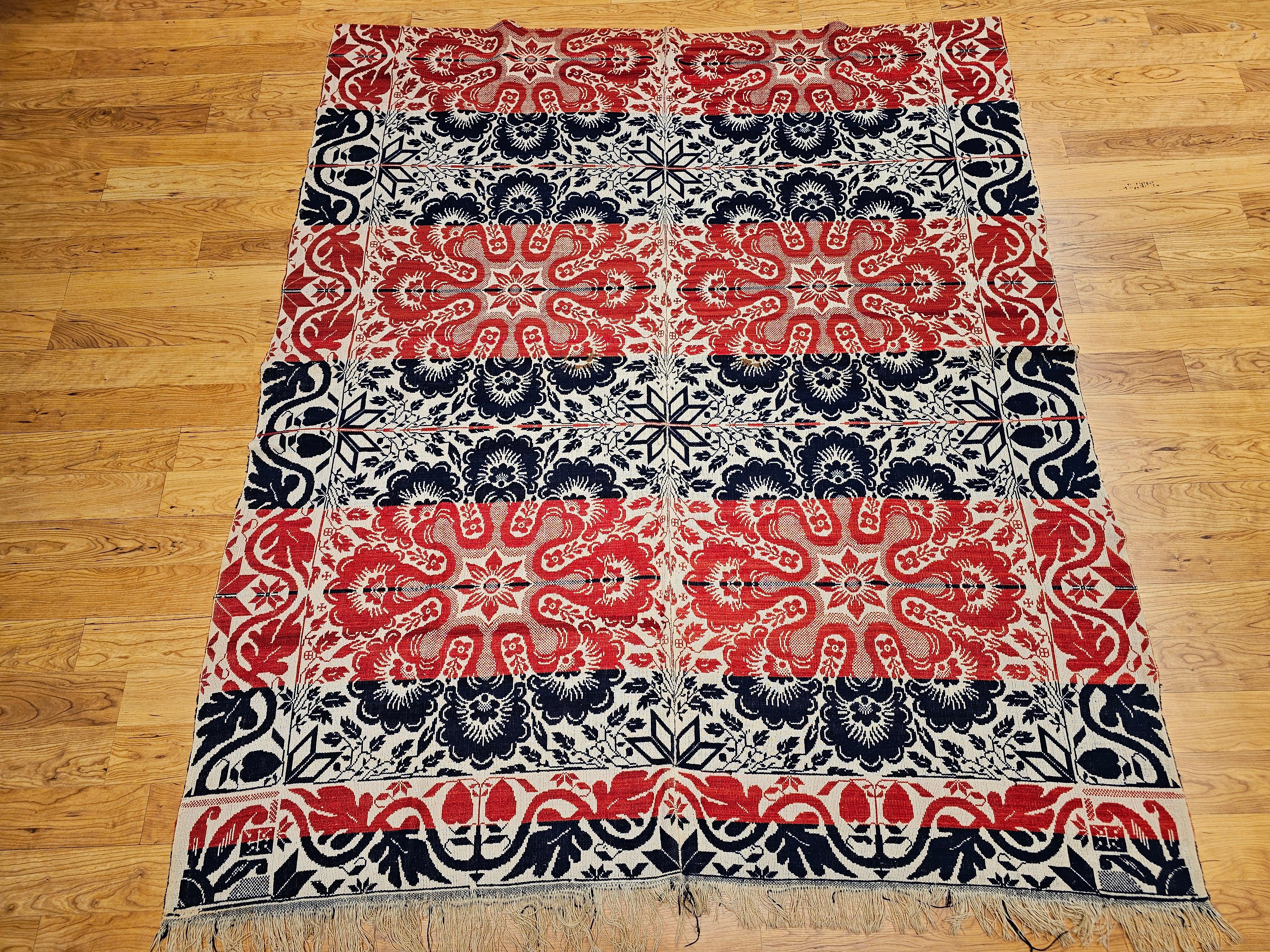 This mid-19th century American tri-color coverlet is a striking example of early American textile craftsmanship, woven in red, blue, and white using a Jacquard loom. Featuring floral medallions throughout the field and a foliate border, the design