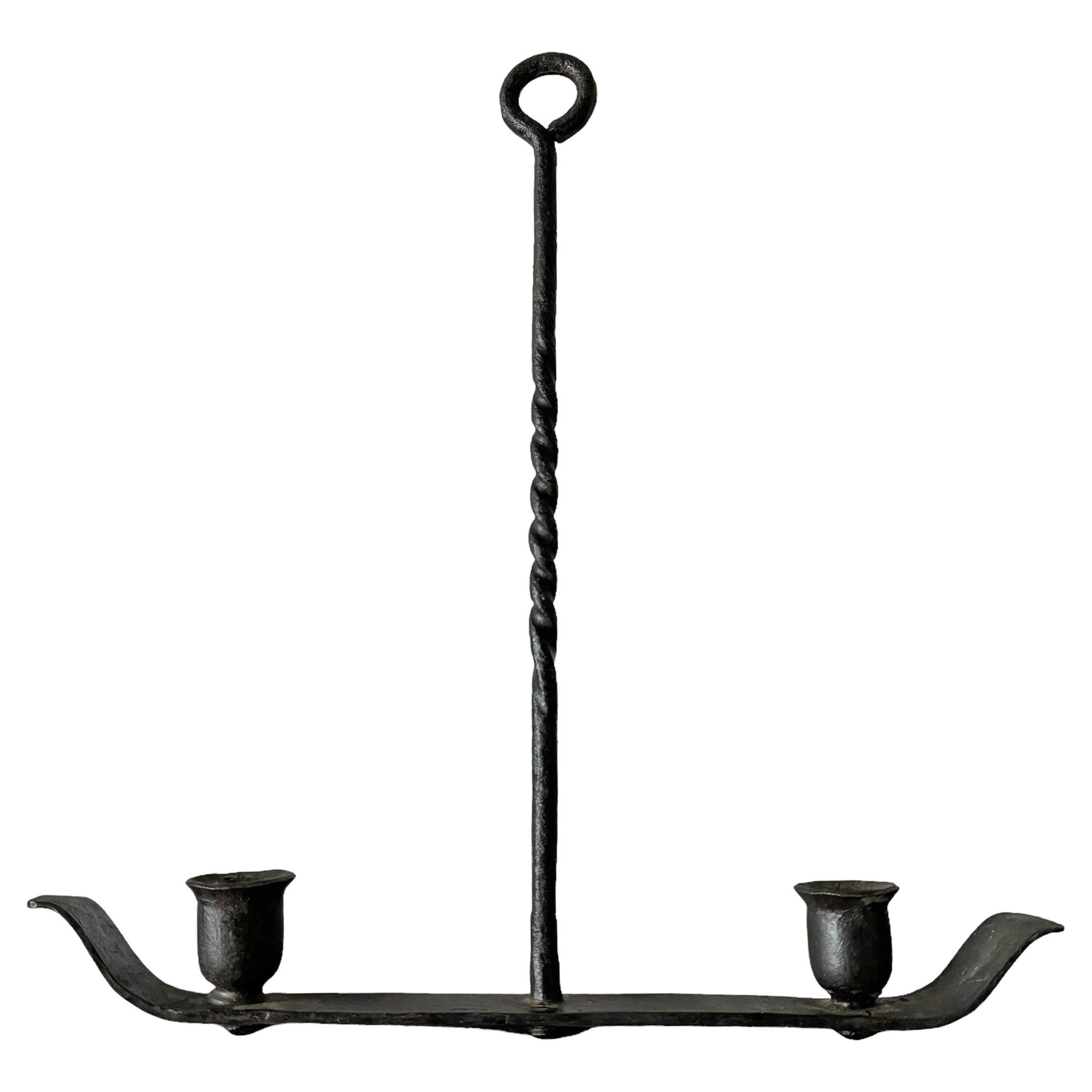 Este candelabro de dos brazos de hierro forjado estadounidense del siglo XIX es una impresionante pieza de artesanía histórica. Presenta un tallo retorcido, que muestra las intrincadas habilidades de herrería, y una barra plana martillada que