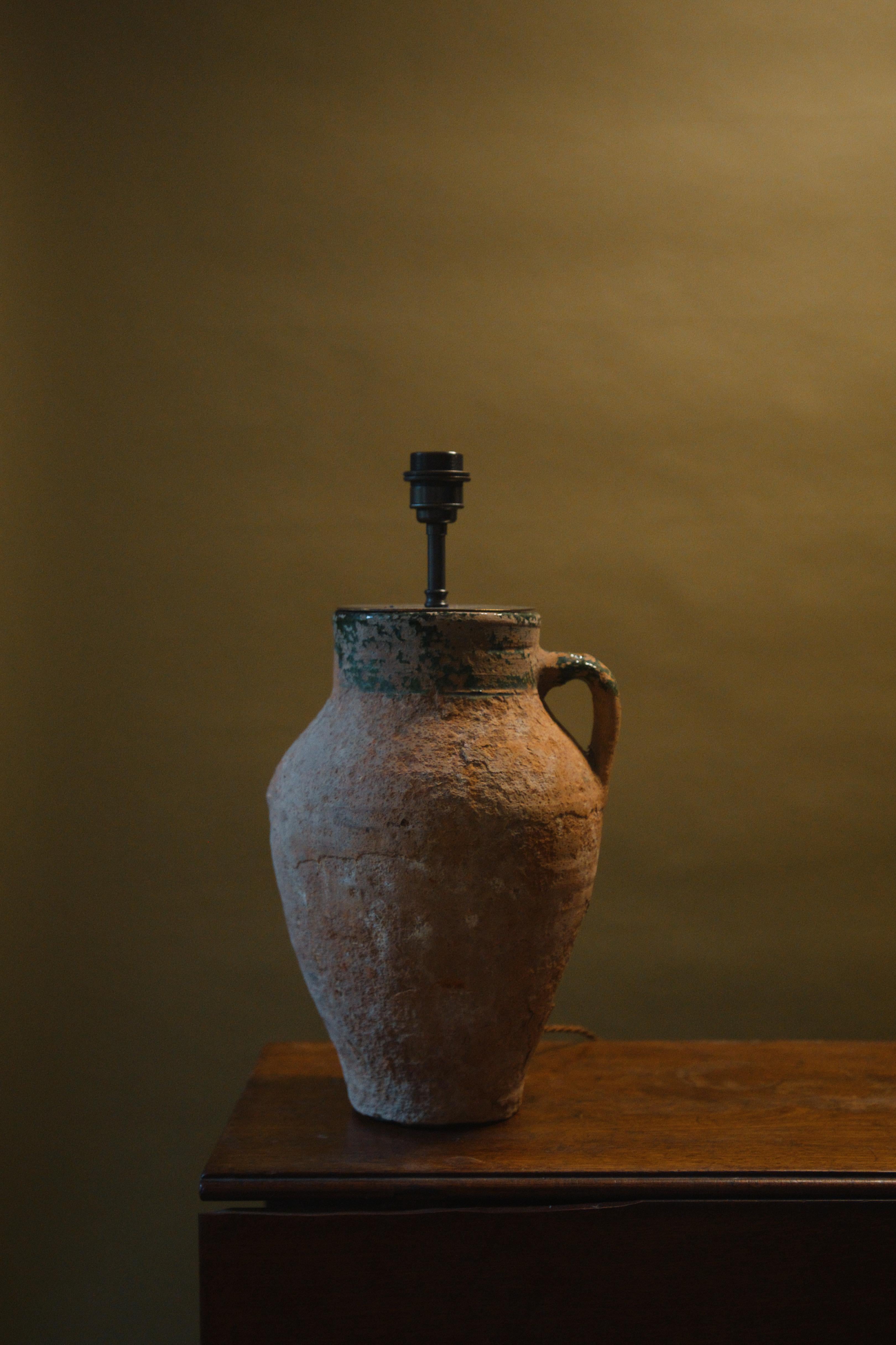 Questa lampada anatolica del XX secolo è uno splendido esempio di artigianato e design senza tempo. Realizzato a mano a partire da un vaso d'epoca in argilla mediterranea, la sua esclusiva finitura smaltata aggiunge un tocco di eleganza e