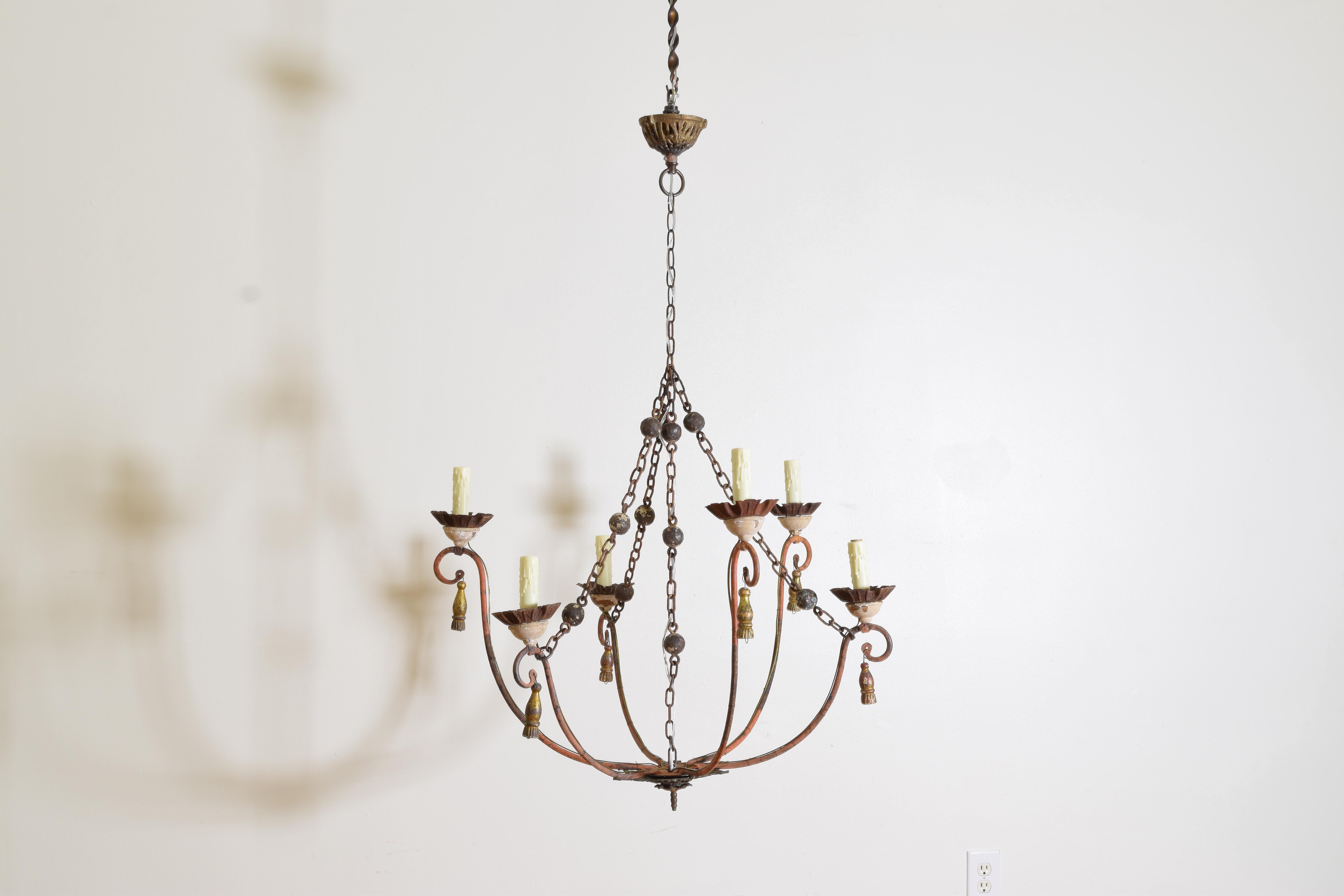 A large red-painted iron chandelier made up of 19th century and later parts with decorative chains and hanging tassels from the carved wooden and iron bobeches.