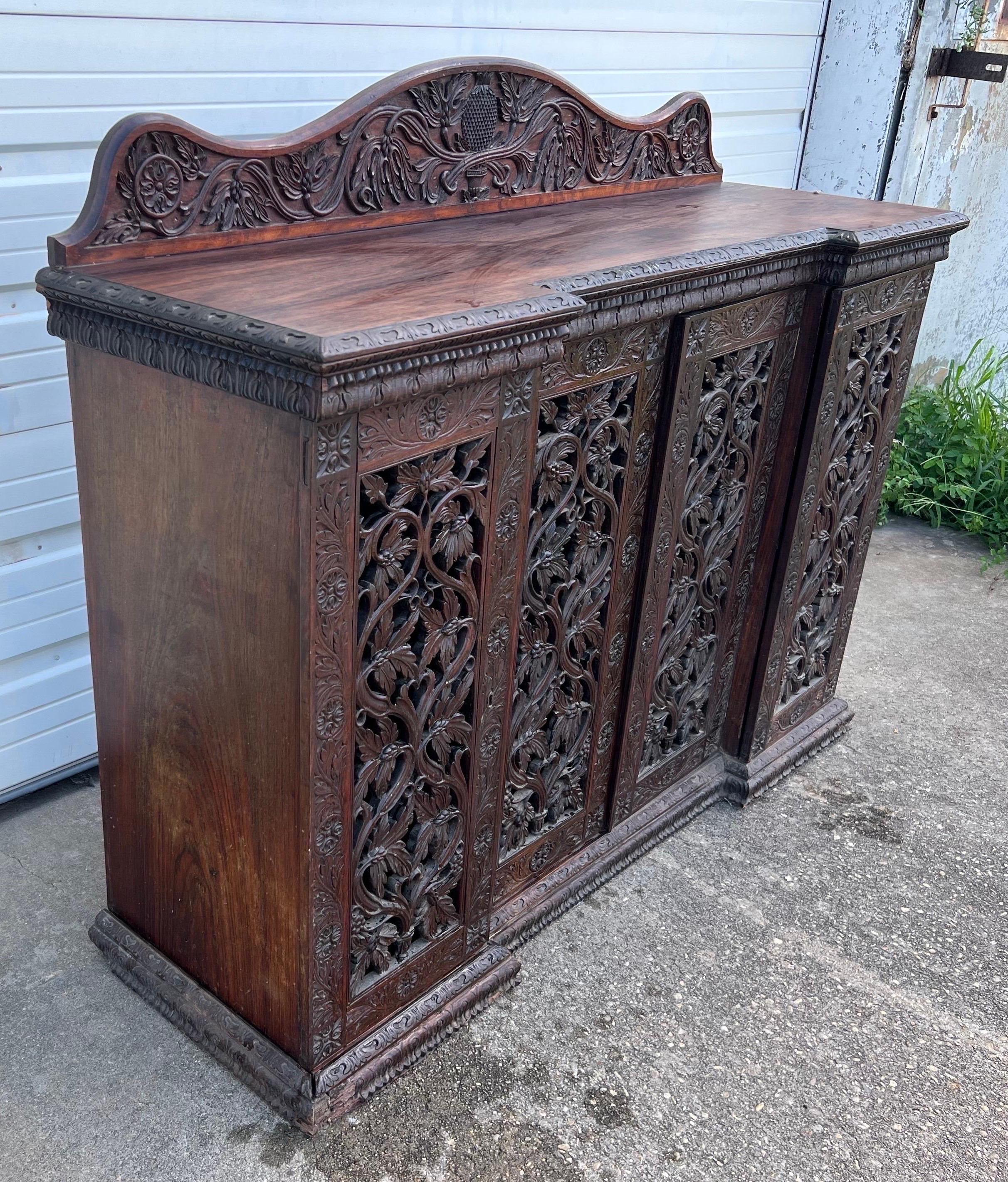 Great quality 19th century Anglo Indian 4 door rosewood credenza with carved pineapple backsplash. Heavily carved doors with hearts and foliage covering the cabinet and shelves. Great for a bar or media storage.