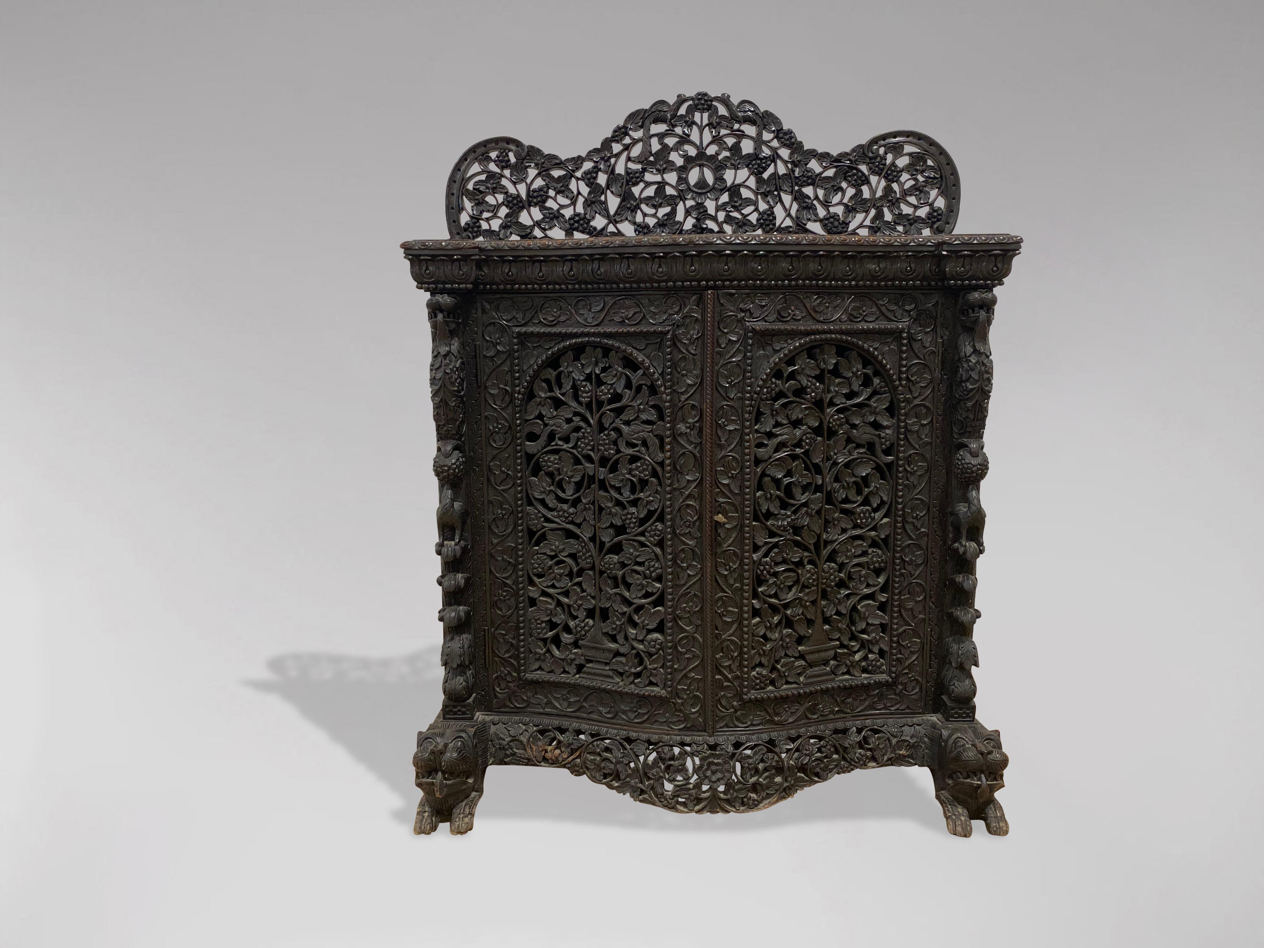 A mid 19th century, Victorian period, British colonial, Anglo-Indian carved and pierced serpentine sideboard with pierced gallery in solid rosewood. The front is mounted with two hinged doors with shaped panelled doors enclosing one long shelf. All