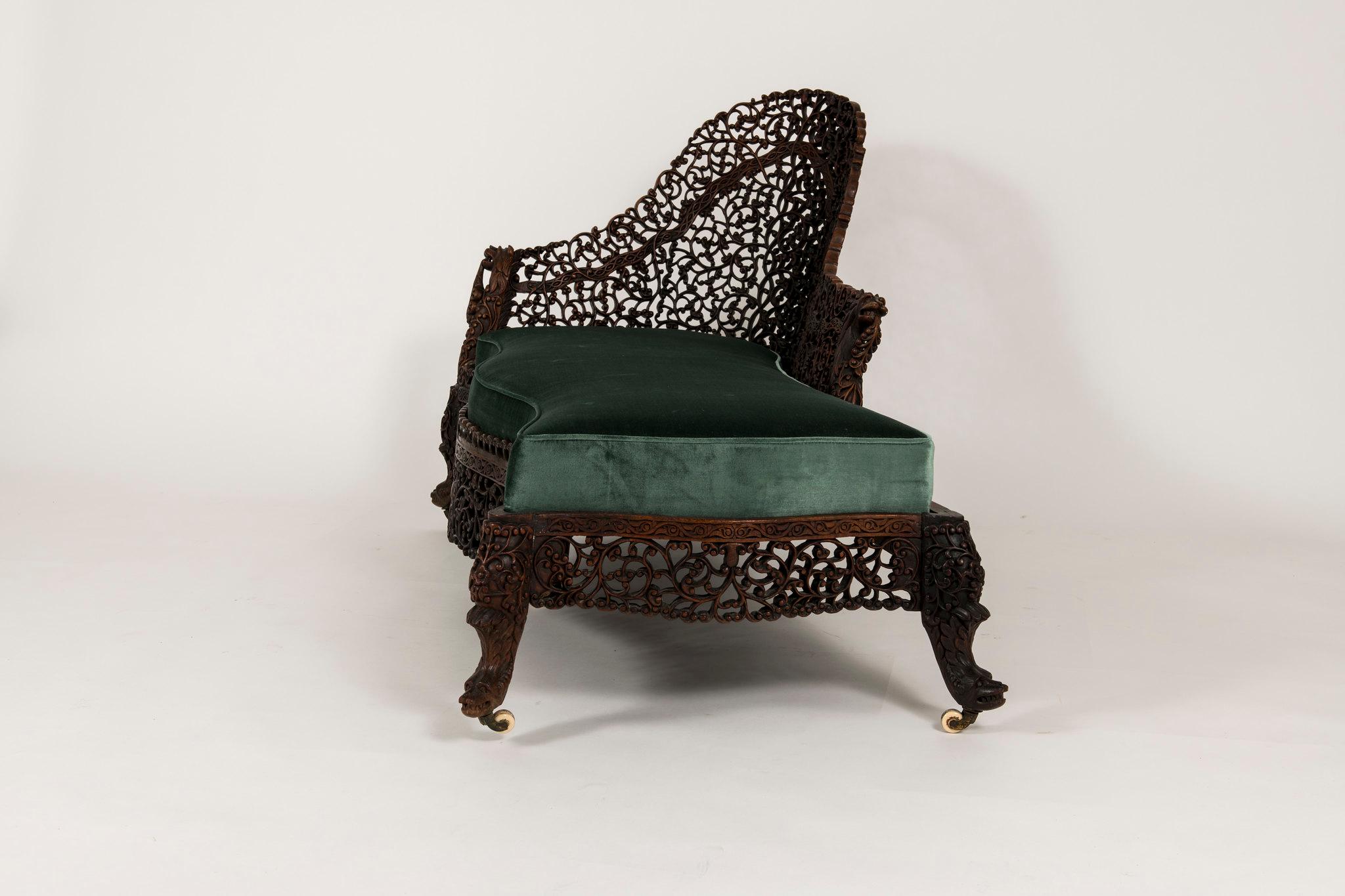 This is a beautifully carved sculptural rosewood Anglo-Indian chaise featuring intricately carved floral-foliage fretwork, mythical beasts at casters, a lion's head armrest and a newly upholstered seat in a teal Italian silk velvet.
