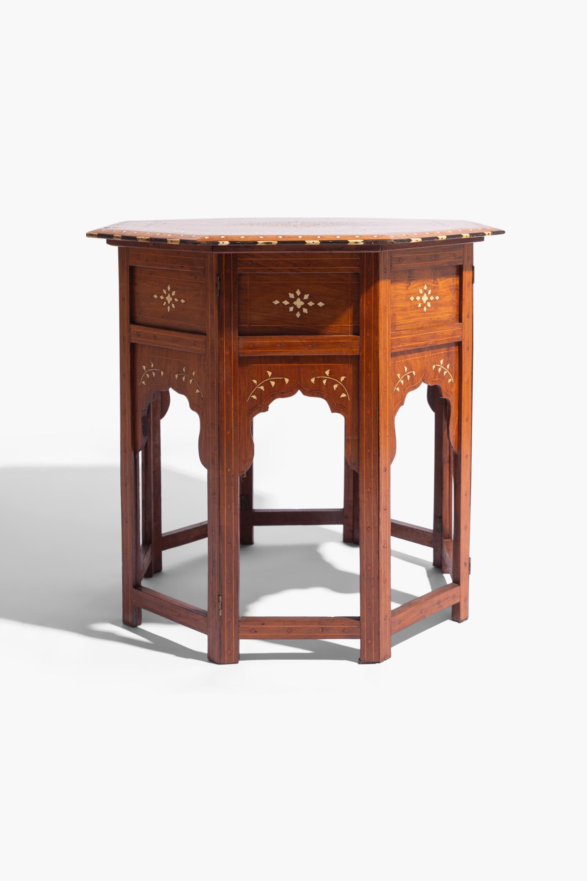 Table centrale en bois de santal incrusté d'os du 19e siècle. Le plateau octogonal avec une bordure de feuillage et un centre à motif étoilé repose sur une base à panneaux pliants.

Bon état d'origine. Petites pertes sur la marqueterie correspondant