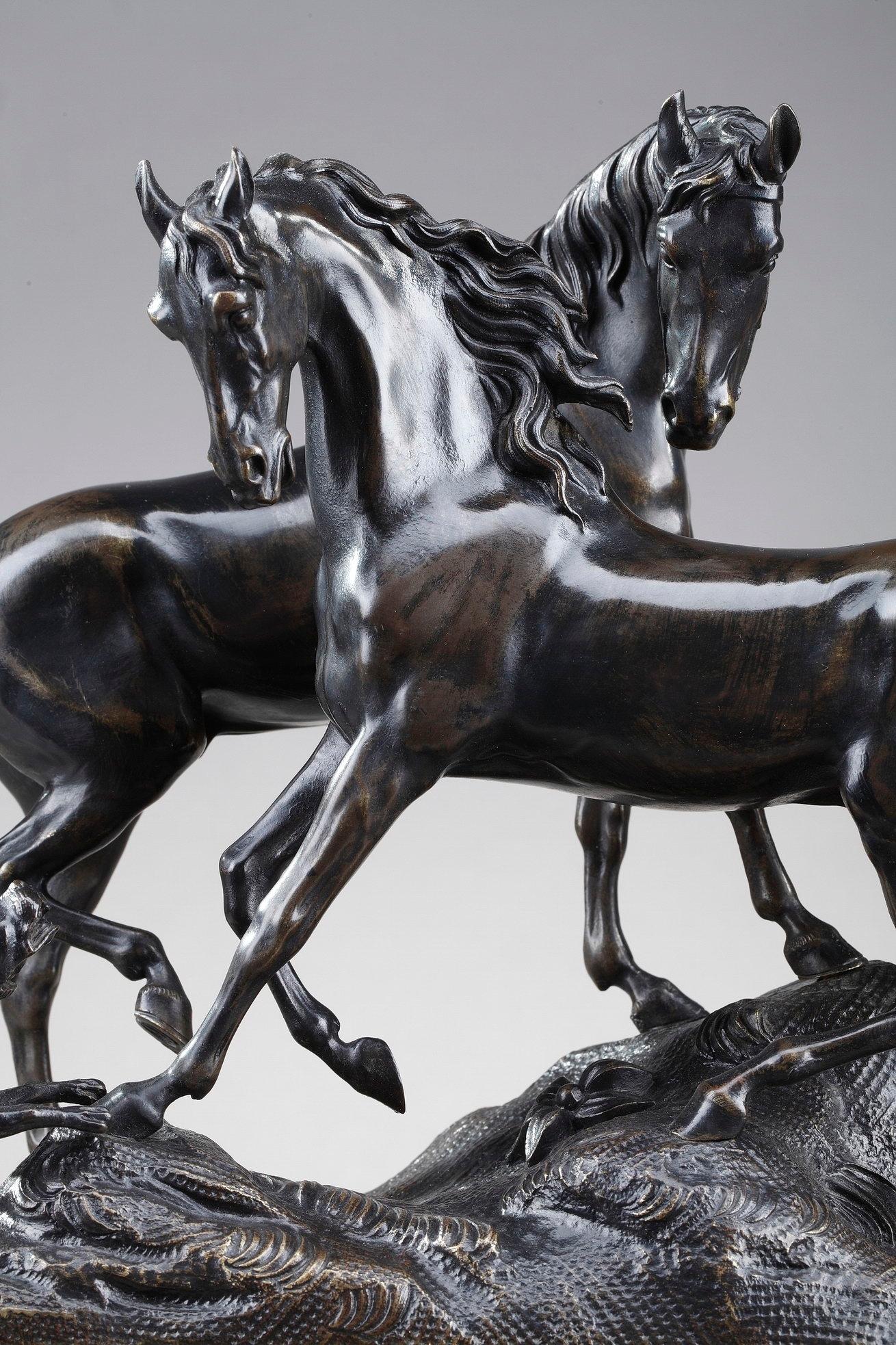 Sculpture en bronze à patine brune L'accolade représentant deux chevaux et un chien se serrant l'un contre l'autre sur un socle naturaliste rehaussé de fleurs. Le chien aboie après les chevaux. Le groupe repose sur une base cannelée en bronze doré