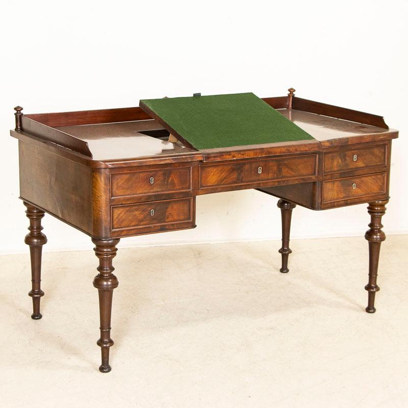 Distinctive and elegant, this English mahogany writing desk has 5 functioning drawers in addition to a unique raised writing/reading surface still covered in green felt. Please enlarge photos to appreciate the attractive rich mahogany grain. There