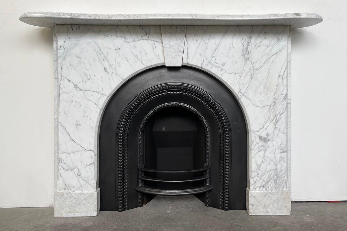 An arched Victorian fireplace surround of good proportions in well-figured pencil vain Carrara marble. The carved edge of the serpentine mantle returns back into the wall allowing it to fit on a narrower chimney breast than the overall width of the