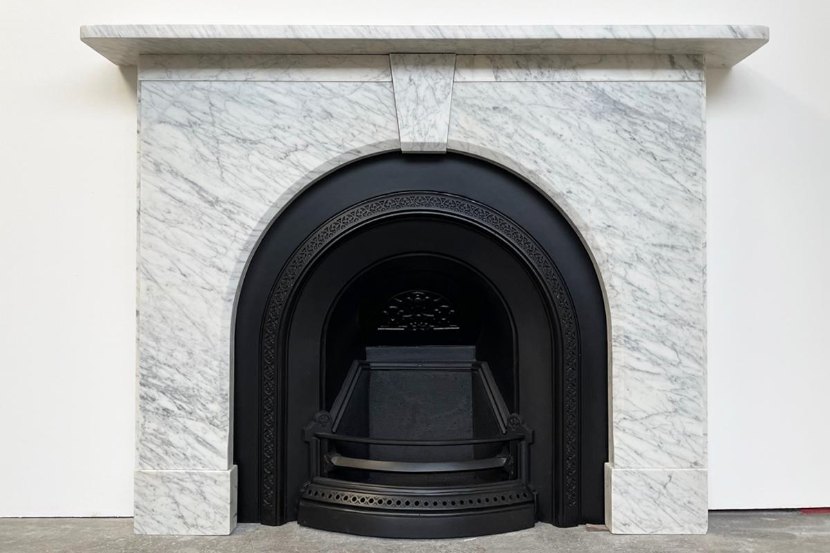 An arched Victorian fireplace surround of good proportions in well-figured pencil vain Carrara marble. The simple form benefits from a chamfered inside edge and a plain frieze below the shelf flanking the unadorned keystone. Circa 1860.

Pictured