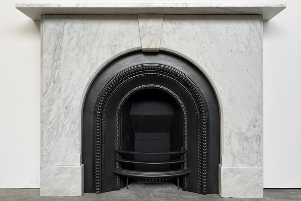 An arched Victorian fireplace surround of good proportions in well-figured pencil vain Carrara marble. The simple form benefits from a chamfered inside edge and plain jambs below the shelf flanking the unadorned keystone. Circa 1860.

Pictured with