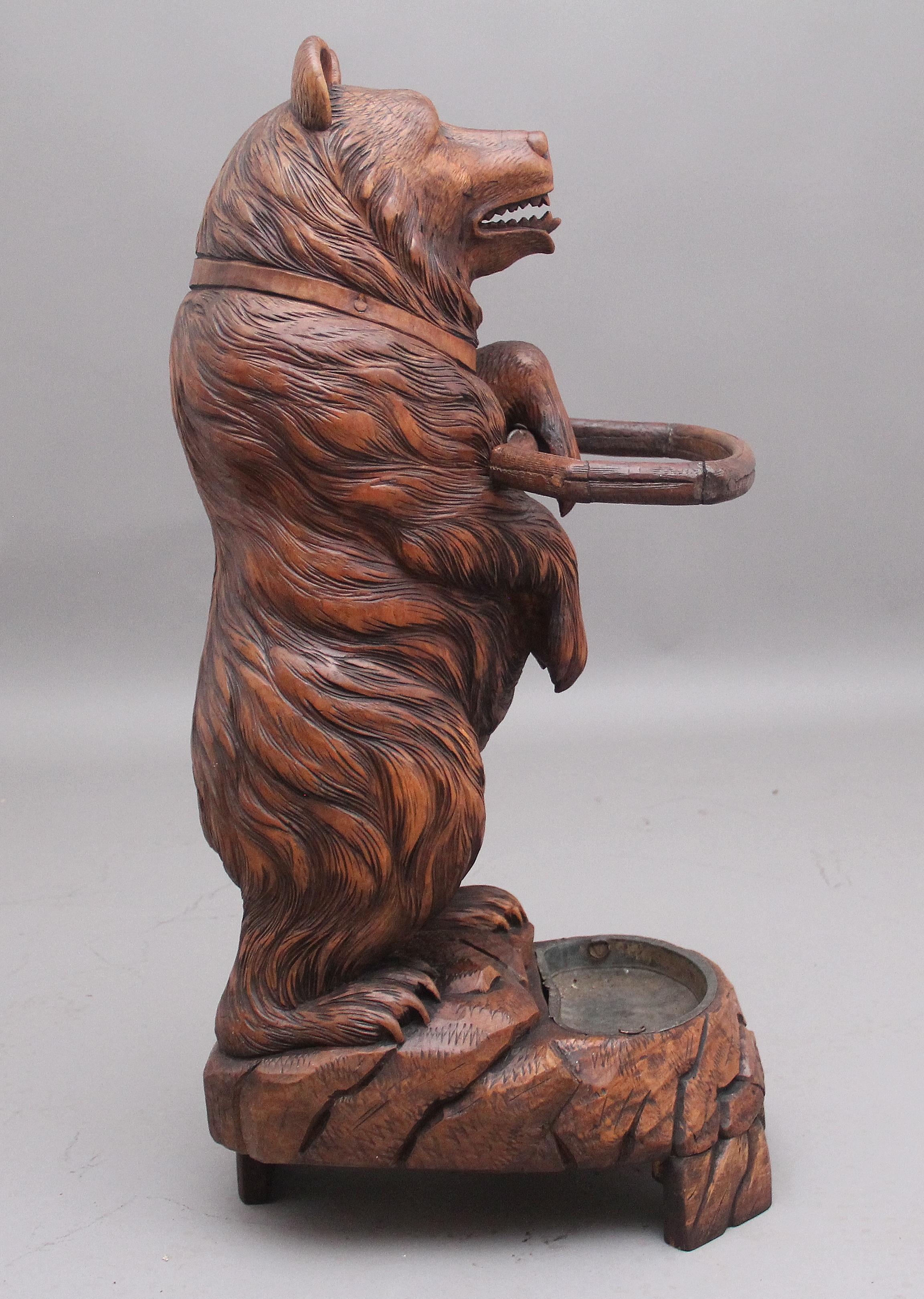 19th century black forest bear stick/umbrella stand constructed in linden wood, the stand consisting of a bear standing on his back legs with a front paw extended, with a naturalistic rockwork base inset with a drip pan, lovely quality carving and