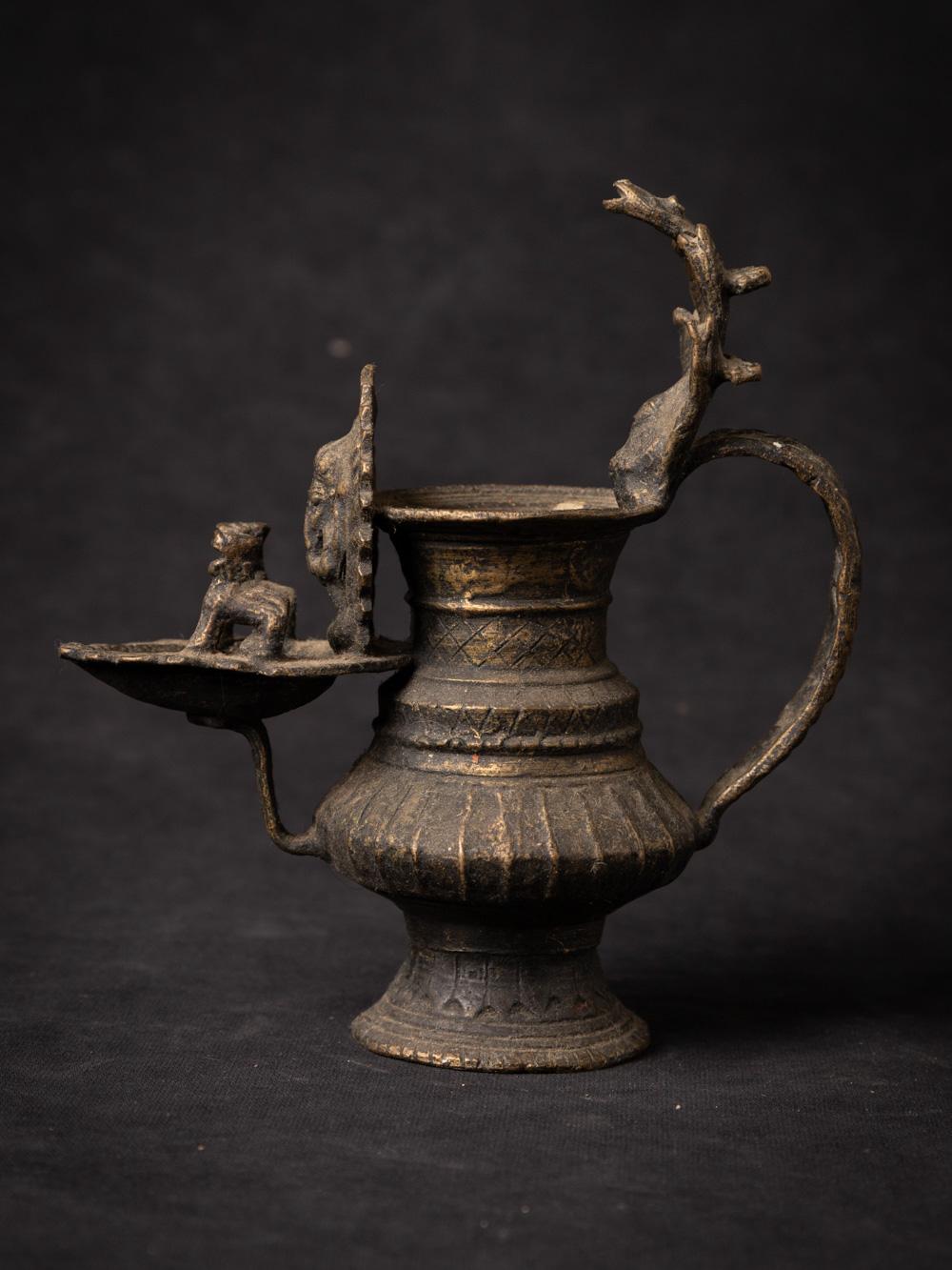 This antique bronze Nepali oil lamp carries within it a sense of history and cultural significance. Crafted from sturdy bronze, the lamp stands at a height of 16.1 cm with dimensions of 7 cm in width and 14.8 cm in depth. Its compact yet intricate