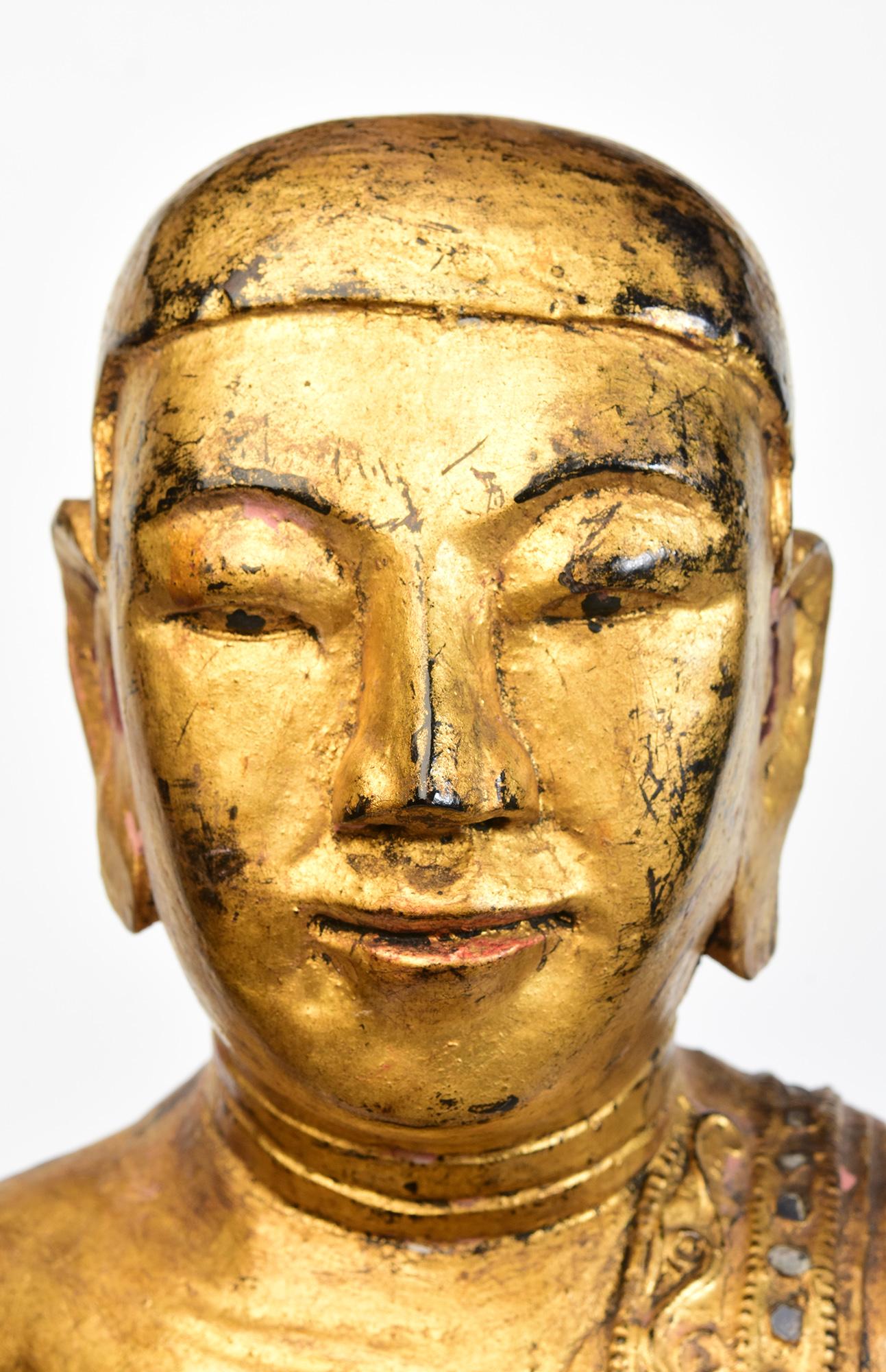 Antique Burmese wooden standing disciple holding bowl with gilded gold and inlay of colorful glass pieces on the borders of the robe. 

Age: Burma, Mandalay Period, 19th Century
Size of disciple only: Height 60.2 C.M. / Width 35.3 C.M. / Depth 14.2