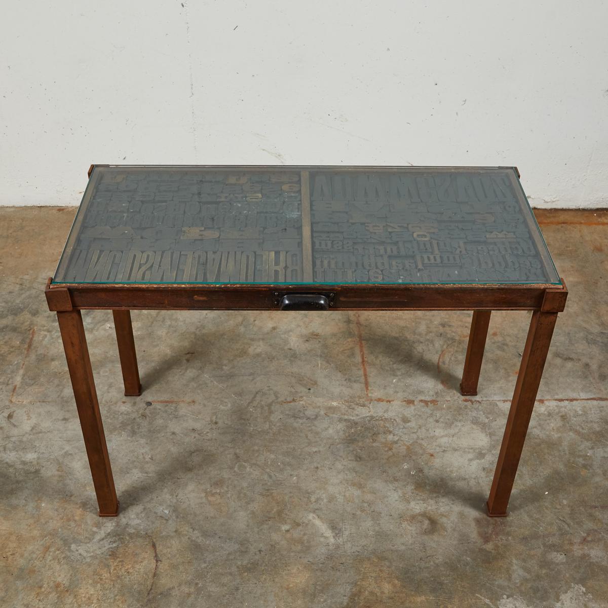 Industrial glass top table with graphic lettered top. The table began its life as a typeface tray in late 19th-century France. Having since been mounted on rectangular iron legs and given a glass top, the table's design reflects its industrial