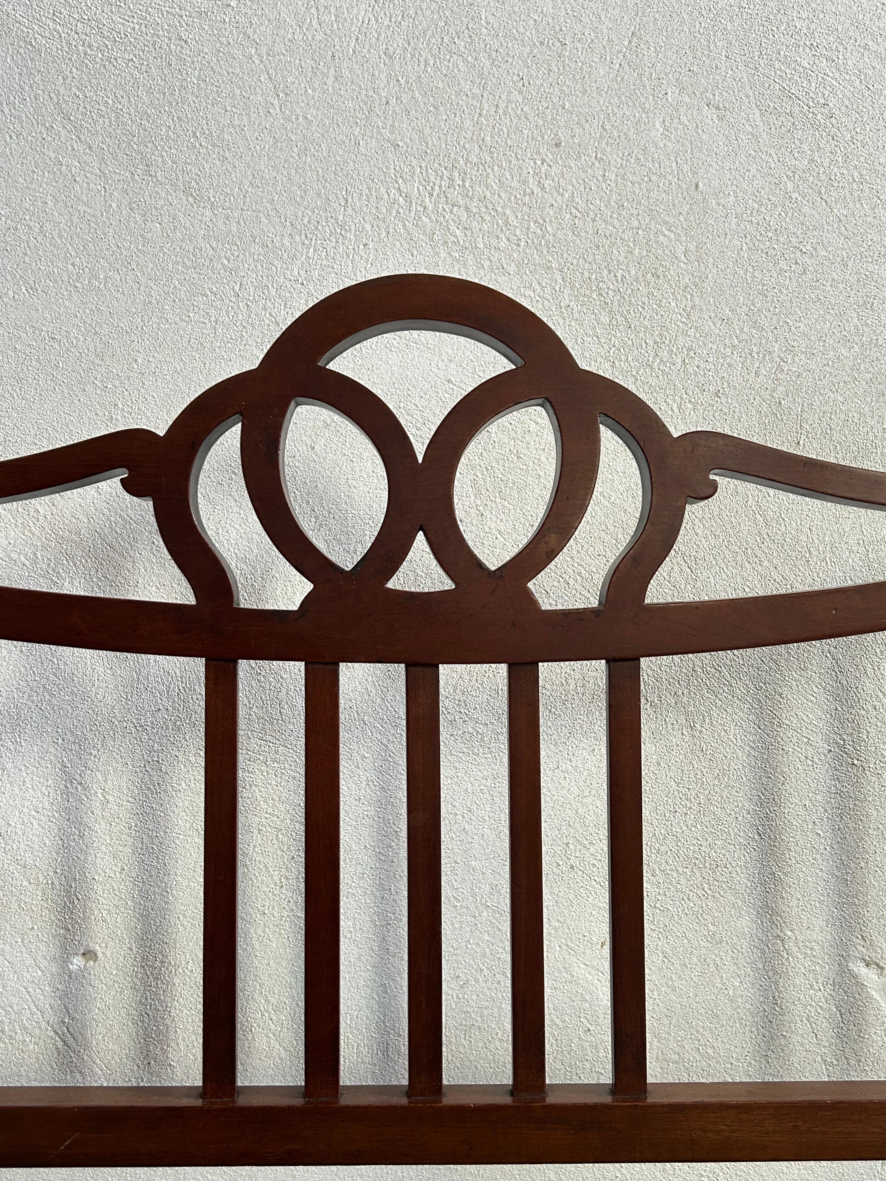 Un banc raffiné et élégant de style Eleg, fabriqué en acajou riche et doté d'un dossier magnifiquement incurvé et détaillé. Le design symétrique est mis en valeur par un motif décoratif entrelacé au centre, flanqué de délicats supports en fuseau et