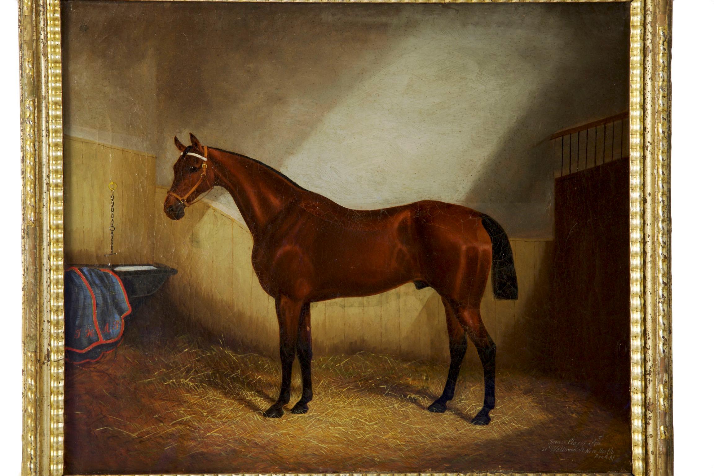 A very fine painting of a show horse with a cropped tail and proud stance in a carefully detailed stable setting. The navy blanket is monogrammed personally 
