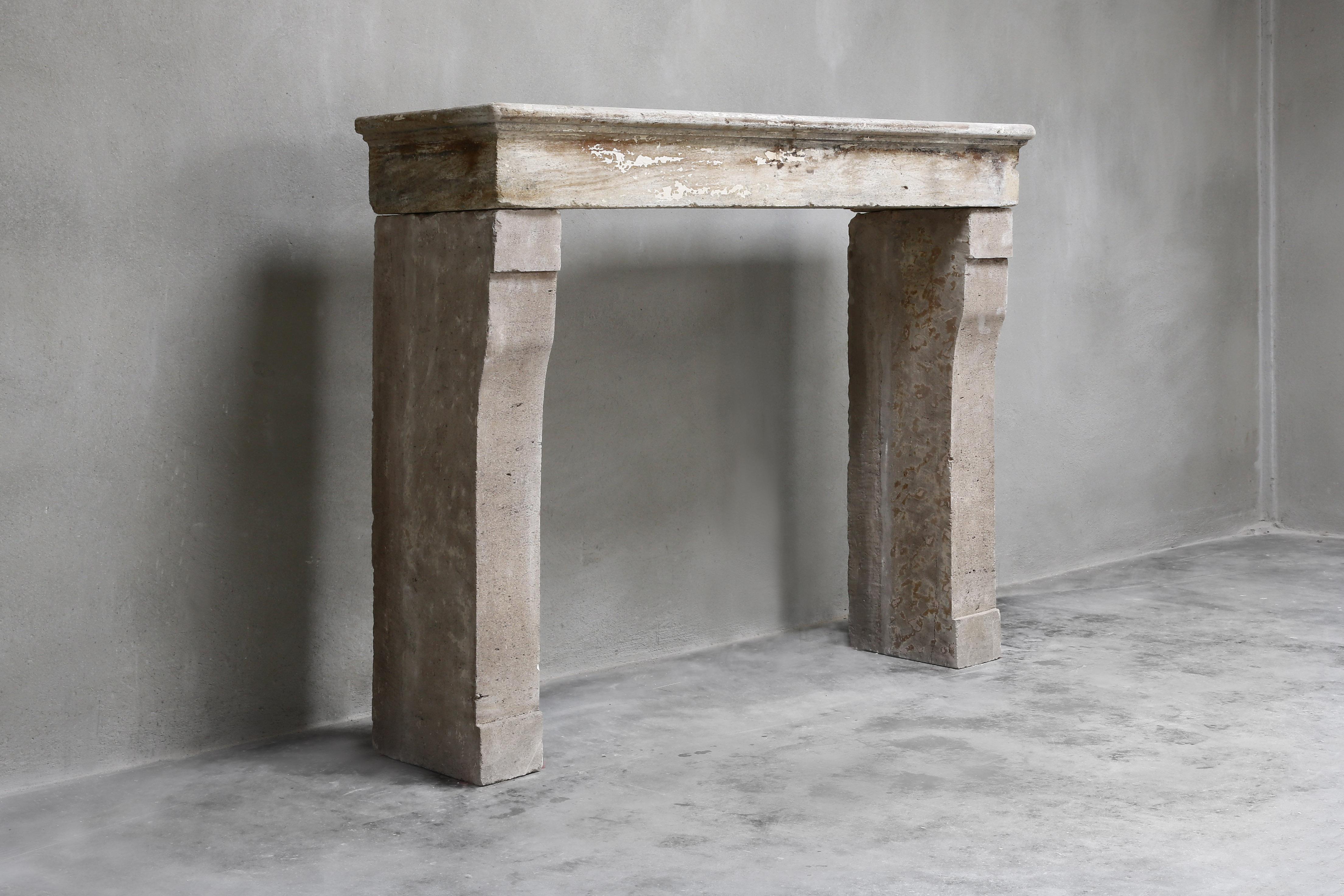 Beautiful sober antique fireplace from the 19th century. A fireplace of French limestone with a straight top and slightly bent legs. The color nuance is warm and there is a beautiful patinae on the fireplace. This fireplace is ideal for rural or