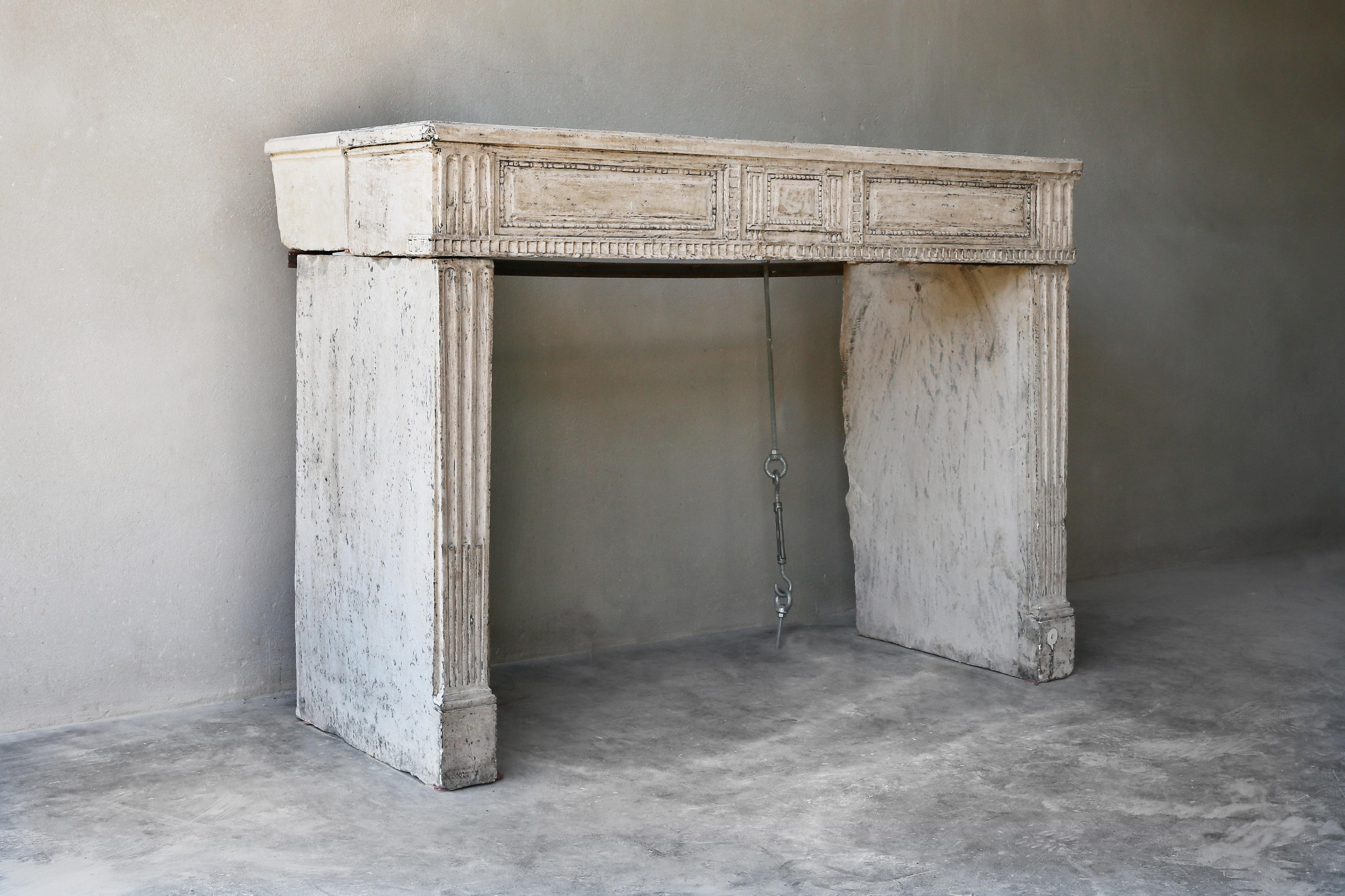 Beautiful patinated antique fireplace of the 19th century. This fireplace is in the style of Louis XVI and made of French limestone. A fireplace with a warm color scheme and cannelures in the front section and on the legs.