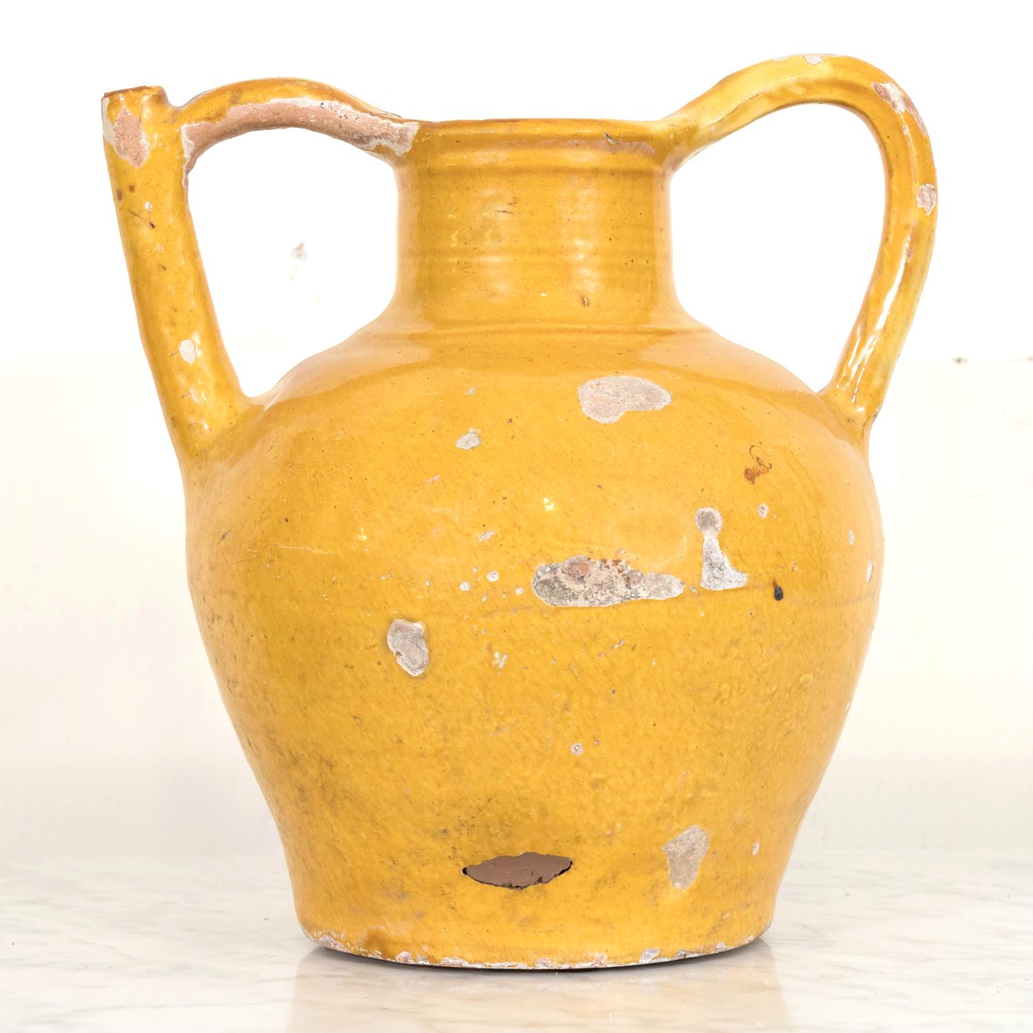 A 19th century French water jug or cruche orjol from the Languedoc region in southwest France, having a mustard yellow glaze and two beautifully arched handles that rise above the opening with the spout formed into the handle on one side, circa