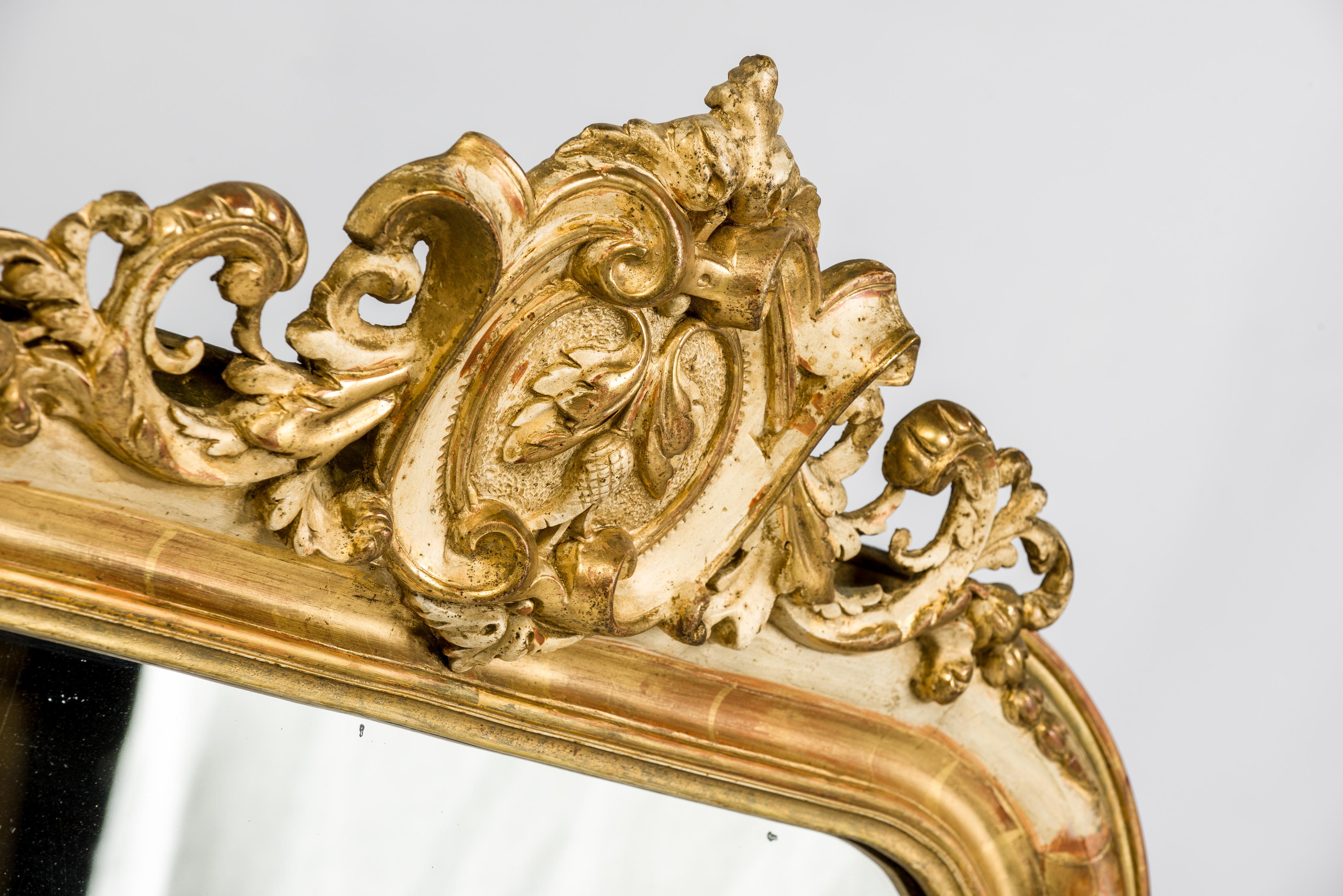 This wonderful antique French mirror has the typical rounded upper corners of a Louis Philippe mirror. The frame is enriched with acanthus ornaments and a beautiful ornate crest on top. 
The frame was partially gold leaf gild and gold paint gilt.