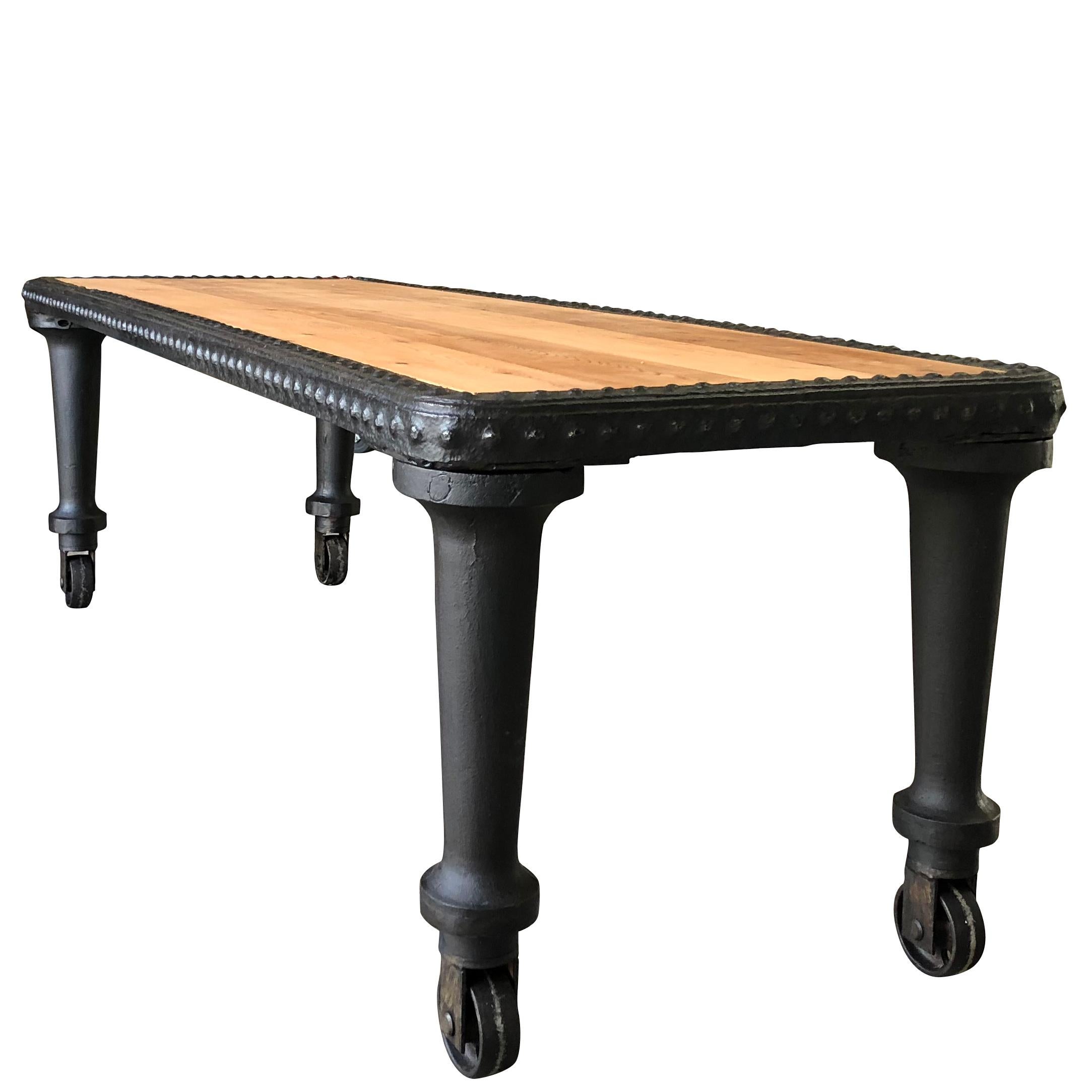 Late 19th century, a very large and heavy Industrial rolling table made of cast iron and steel riveted iron work with a solidly caste iron base on wheels, assembled with large rivets. The table top has been restored with 1.5” thick cedar planks.