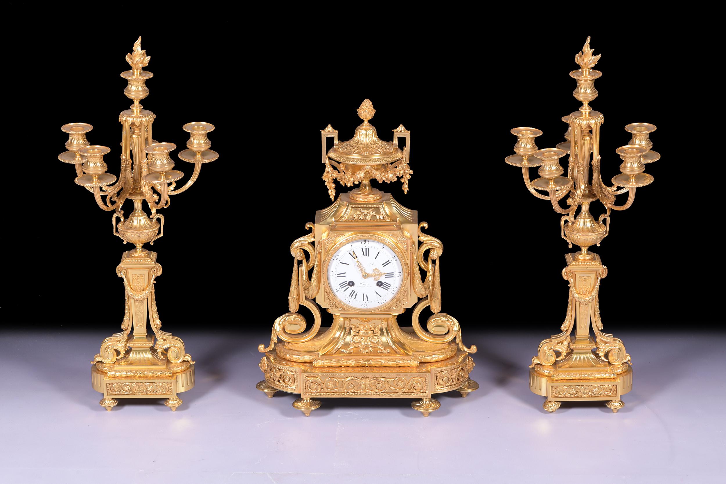 An exceptional quality three-piece clock set designed in a grand neoclassical style by 'Domange Rollin Rue de Bretagne Paris'. France.

The set is comprised of a central clock and two flanking candelabra. The clock features a circular white enamel
