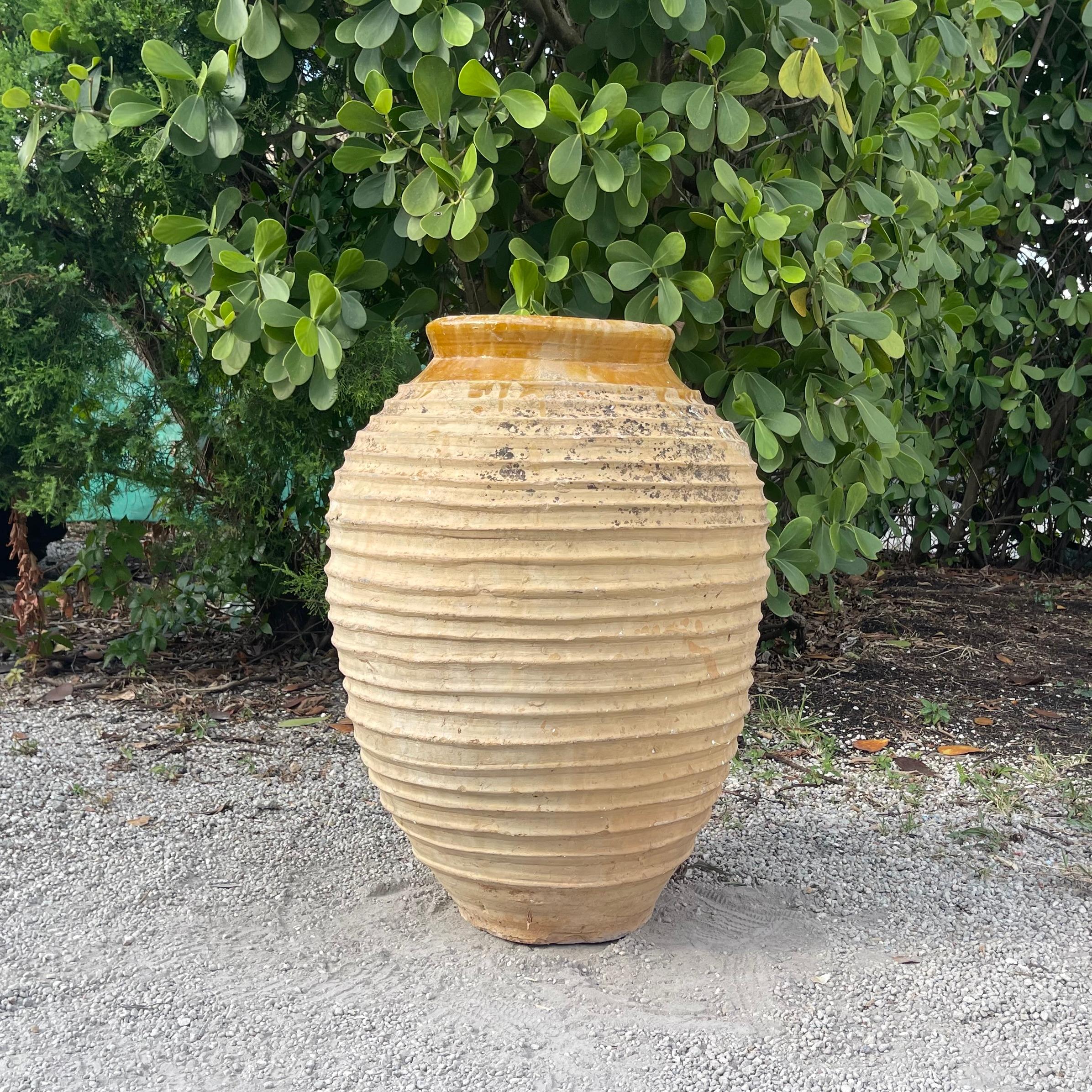 An antique Greek Peloponnese olive oil jar with the typical handcrafted ribbed Nekuma decoration on its round bodice. The rim has a warm yellow glaze. These antique garden pottery vessels were often used for storage and transportation. Minor fading