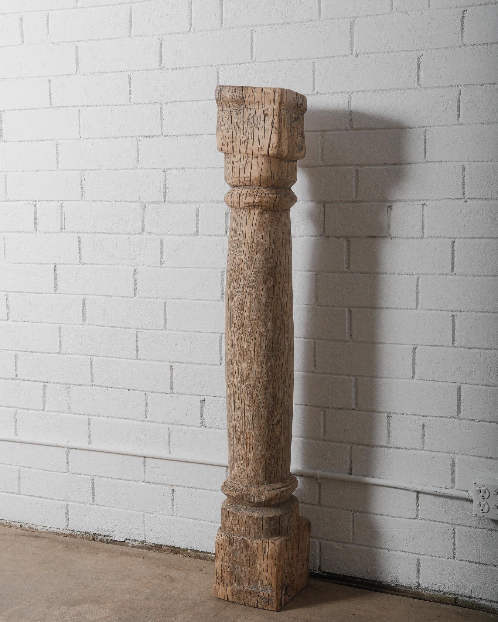 This antique hand-carved teak wood architectural column is a striking piece that embodies the charm of traditional craftsmanship. Originating from the 19th century, this column showcases natural weathering, deep cracks, and a textured surface,