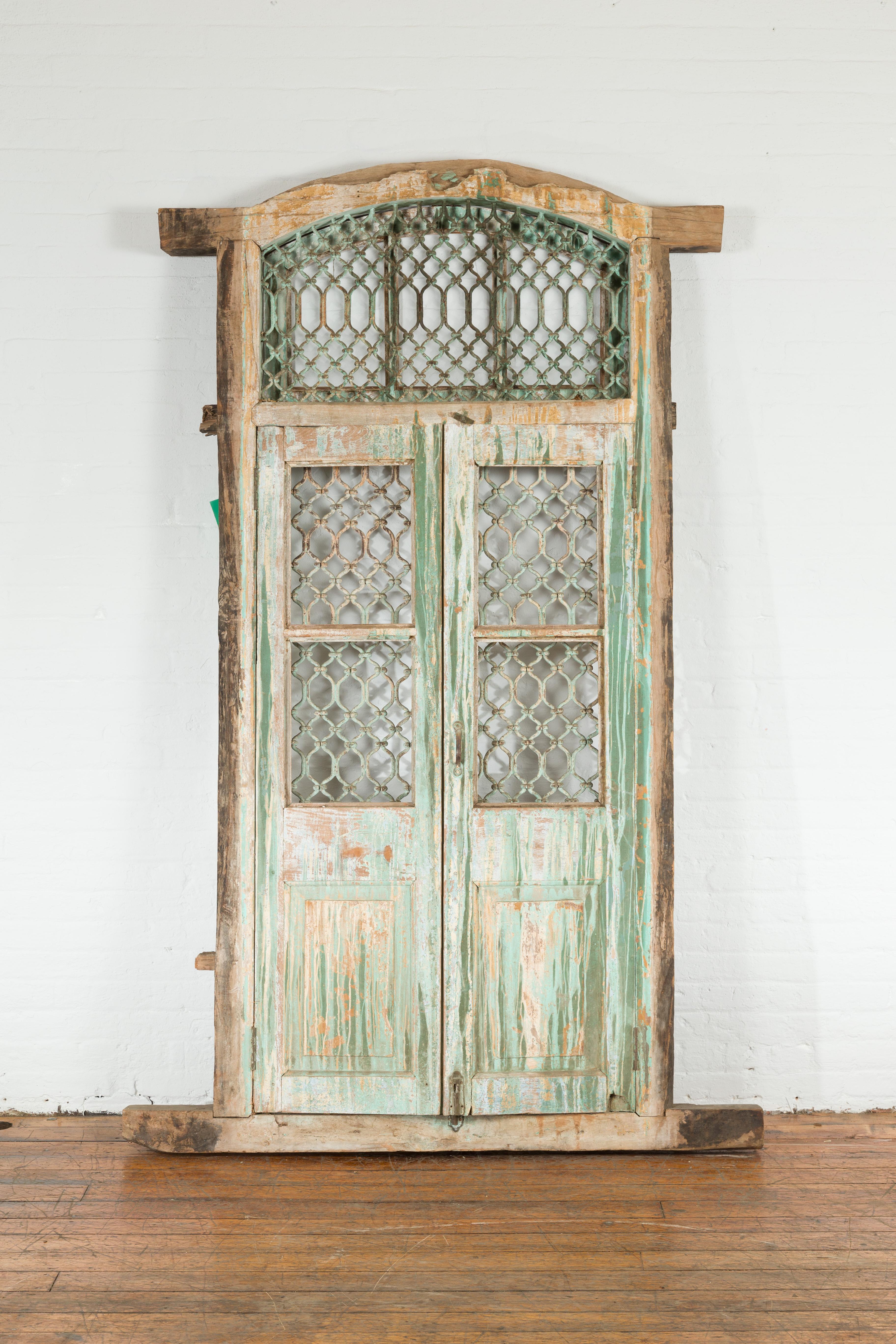 Une fenêtre indienne ancienne en grille de fer du 19ème siècle, avec une peinture verte et une patine d'ancienneté. Créée en Inde au 19e siècle, cette fenêtre haute antique présente une structure en bois joliment vieillie entourant une grille en