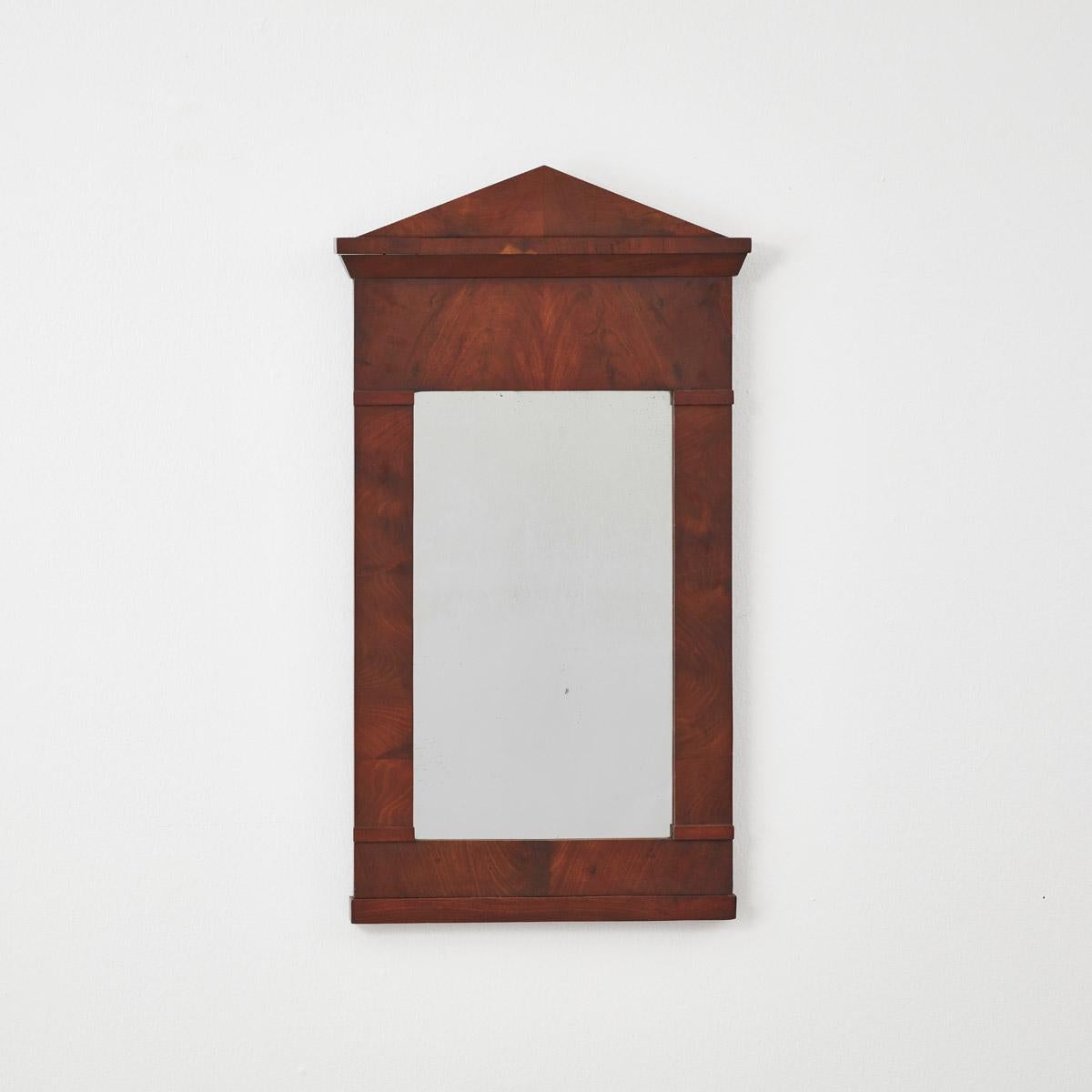 Crafted from rich mahogany, this antique Classical empire style mirror boasts elegance with its bold lines’ characteristic of the neoclassical aesthetic. Its narrow profile makes it ideal for smaller spaces such as a hallway, bathroom or cloakroom. 