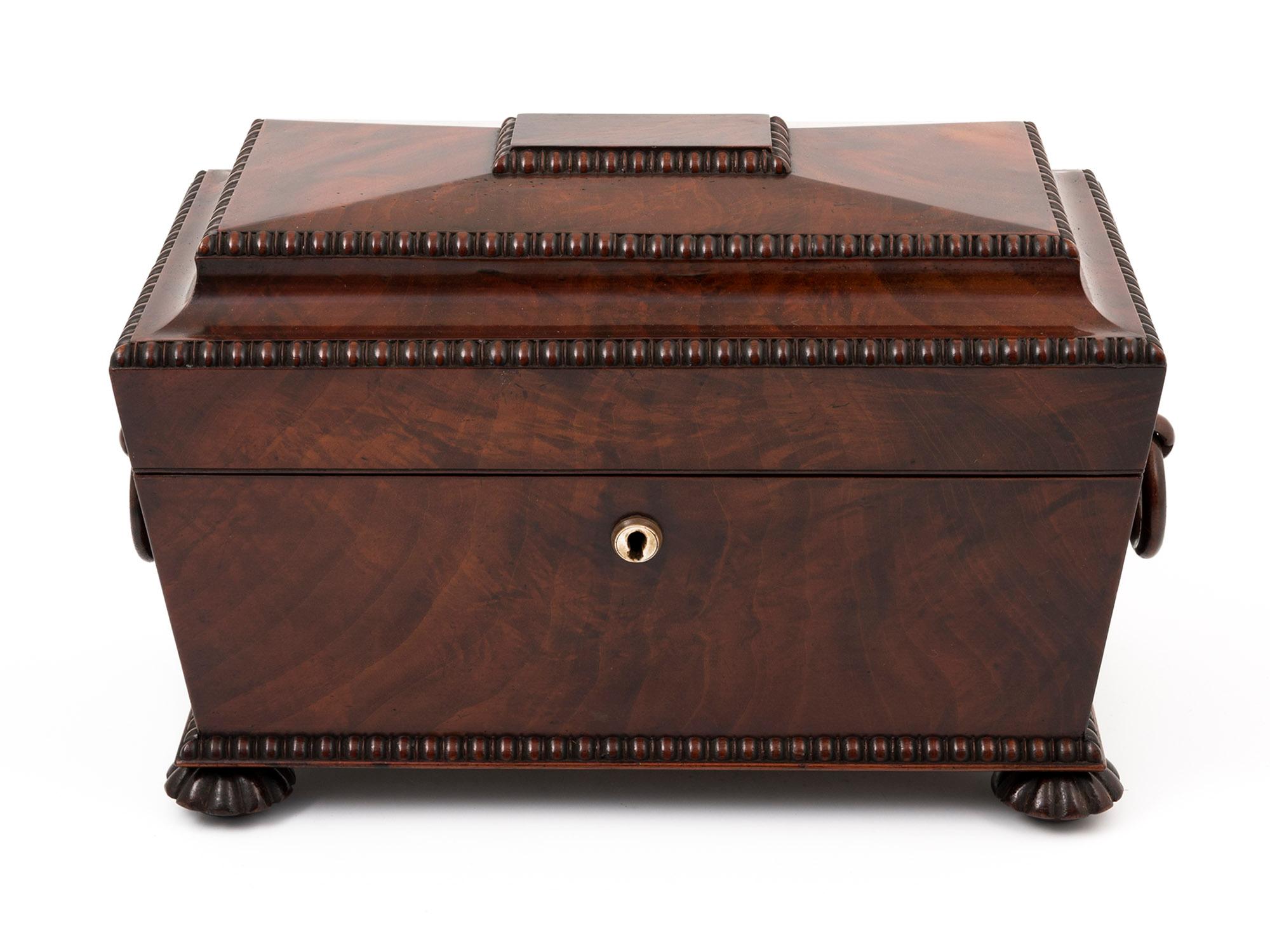 Antique Sarcophagus-shaped tea chest with the original sugar bowl, veneered in stunning flame Mahogany.

This magnificent Tea Chest stands on four turned ribbed feet, with two wooden ring handles on either side and a mother-of-pearl