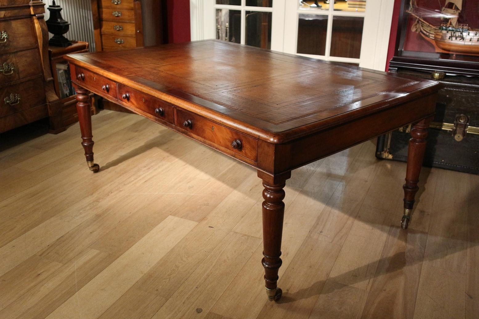 Impressive antique mahogany writing table with 3 drawers on both sides. Entirely in very good condition. Top is inlaid with light brown leather that is richly provided with blind profiling. The wheels no longer roll. This can also be seen as an