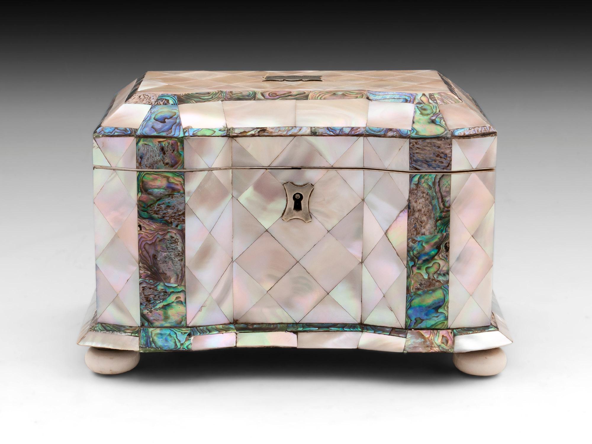 Antique tea caddy adorned with mother of pearl diamonds separated with thick bands of exquisite abalone. Standing on four turned bone bun feet. With an engraved plaque on the top.
The interior features a red velvet backing to the lid and has two