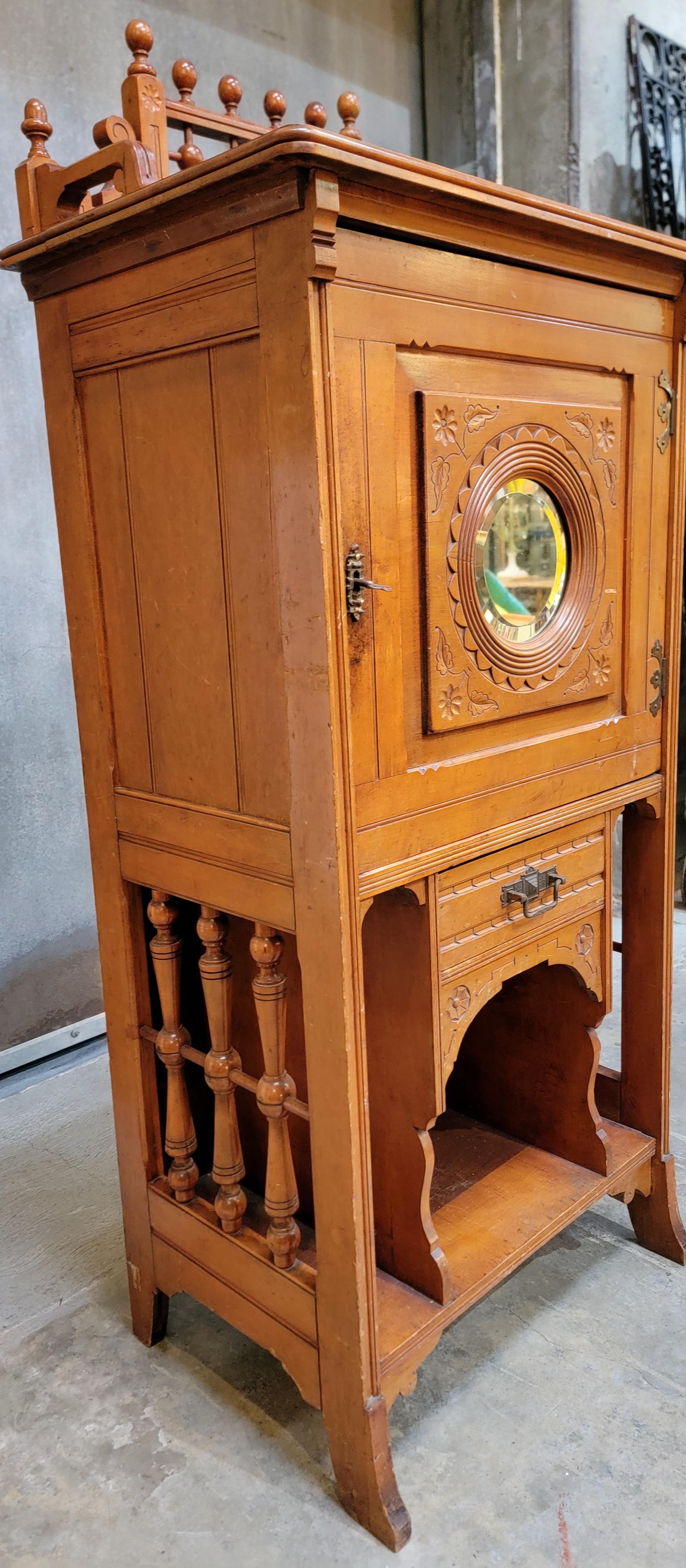 Charming and petite music cabinet with stick & ball detail. Circular beveled mirror on door, shelving to interior of cabinet. Original finish with age appropriate wear and fade. 