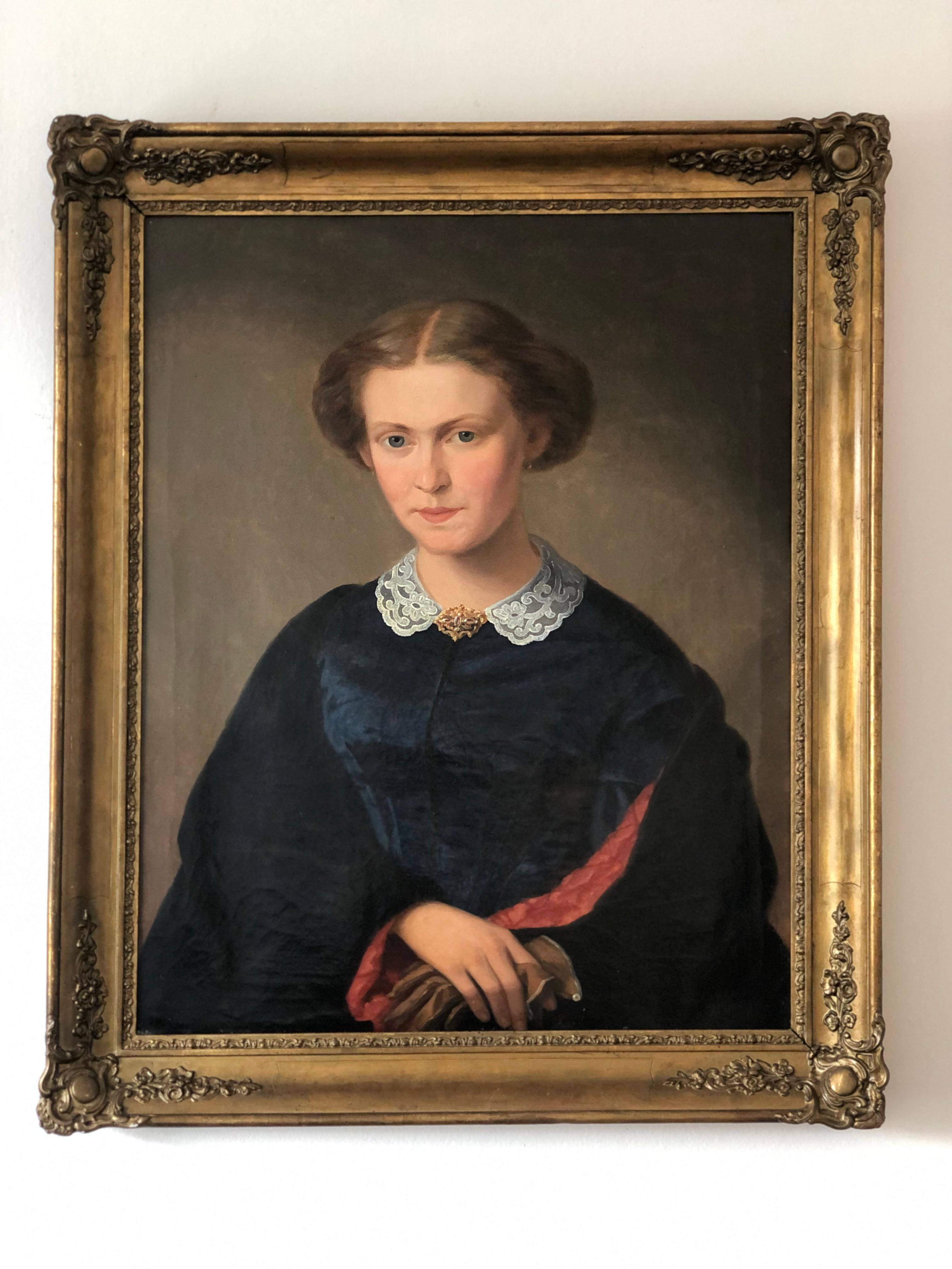 Dieses herausragende Ölporträt aus dem 19. Jahrhundert fängt die ruhige Eleganz einer deutschen Dame ein. Sie trägt ein tiefes marineblaues Kleid mit einem zarten weißen Spitzenkragen und einer goldenen Brosche. Sie verkörpert die elegante