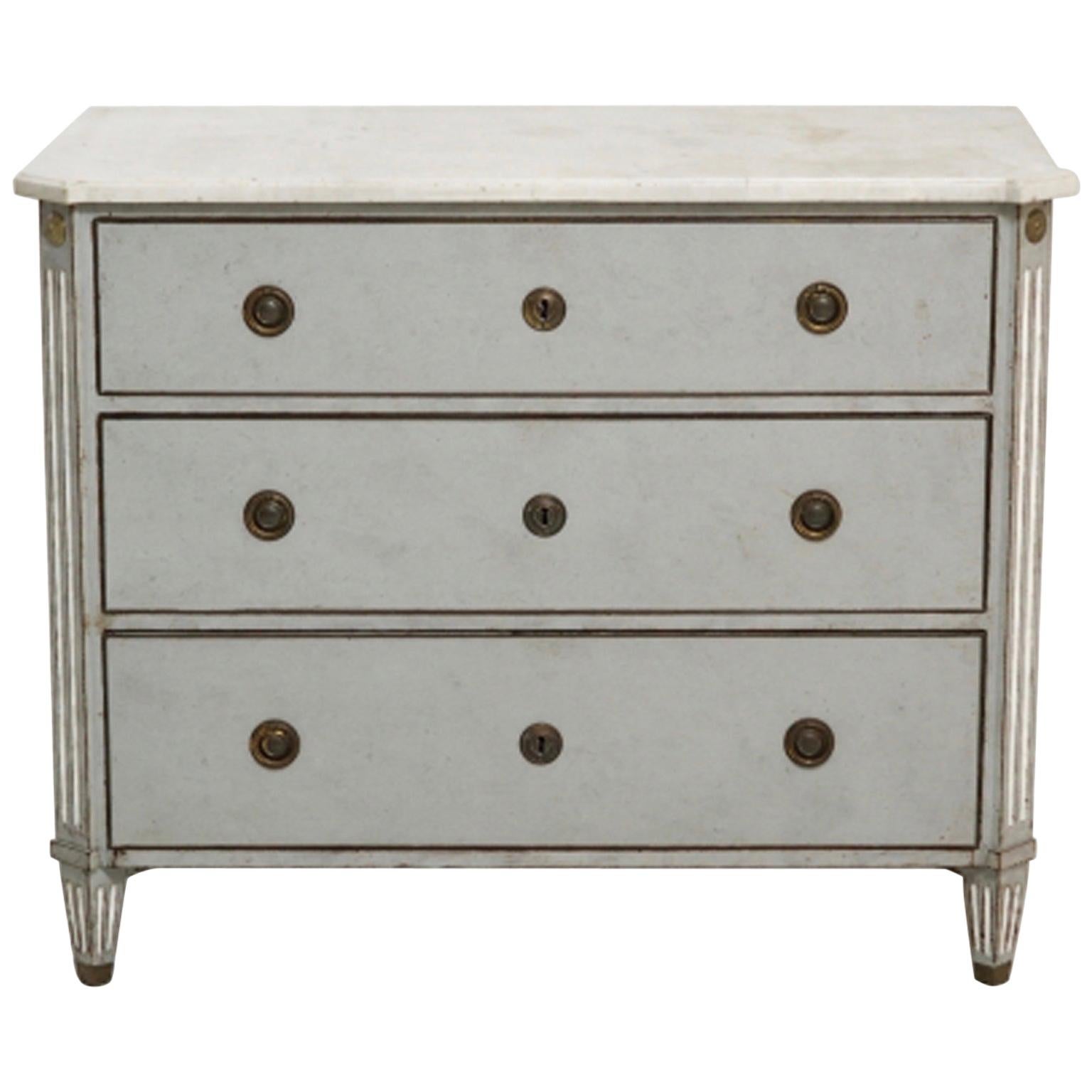 A blue-grey, antique Swedish Gustavian style chest with three drawers, made of hand crafted painted Oakwood and original marble top, hardware and brass inlay. The front of the drawers contains cut corners with fluted carvings and tapered legs, in