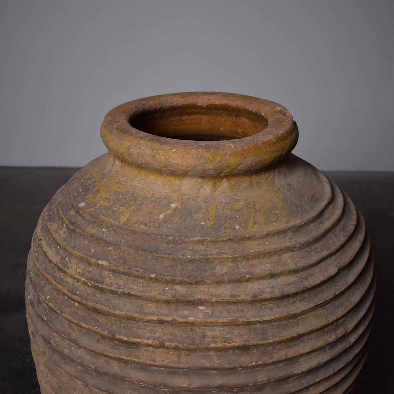 This elegant antique jar was hand-crafted in Greece circa 1860; round in shape with narrow base and neck, the large vessel features a rolled rim at the top accented with a color glaze finish. The wide body is decorated with ribbed ovoid motifs in